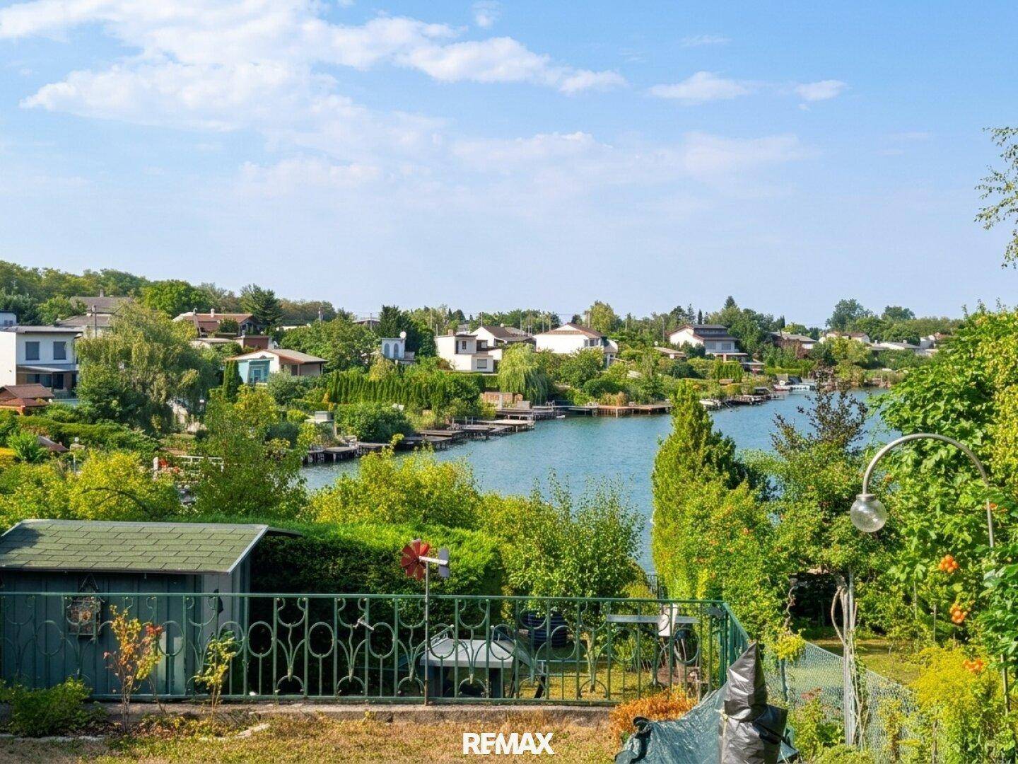 Weitläufiger Gartenbereich mit Rasenfläche, Gartenhaus und Panoramablick auf den See.