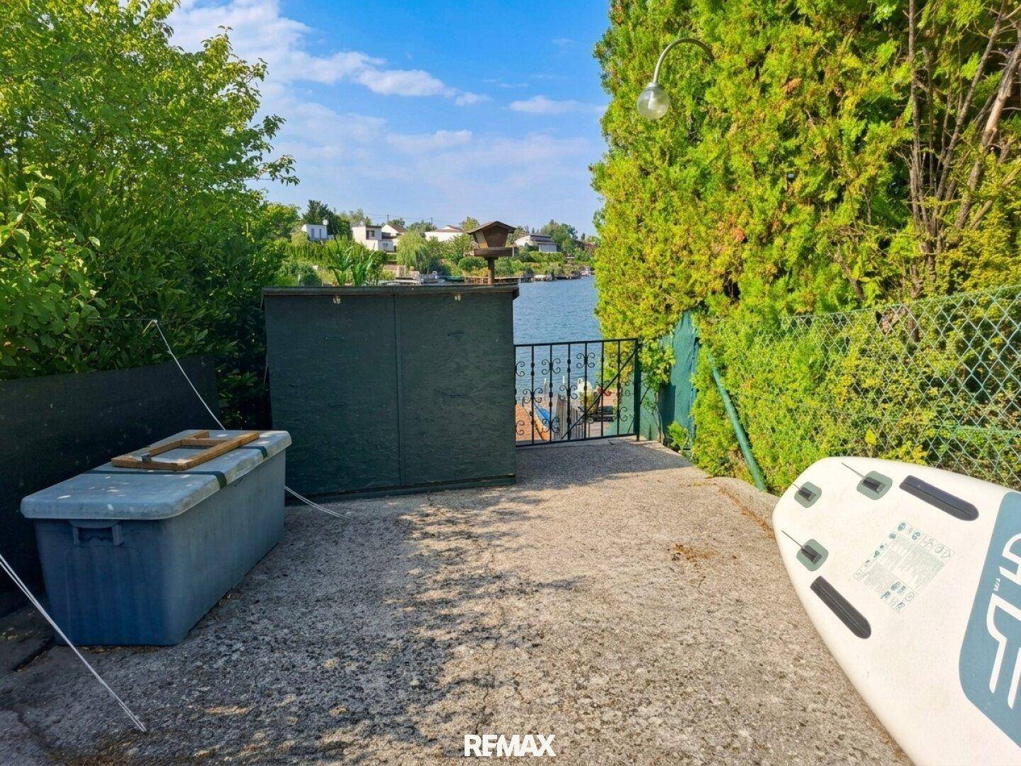 Weg zum Seeufer mit Abstellmöglichkeiten und Blick auf das Wasser unter blauem Himmel.
