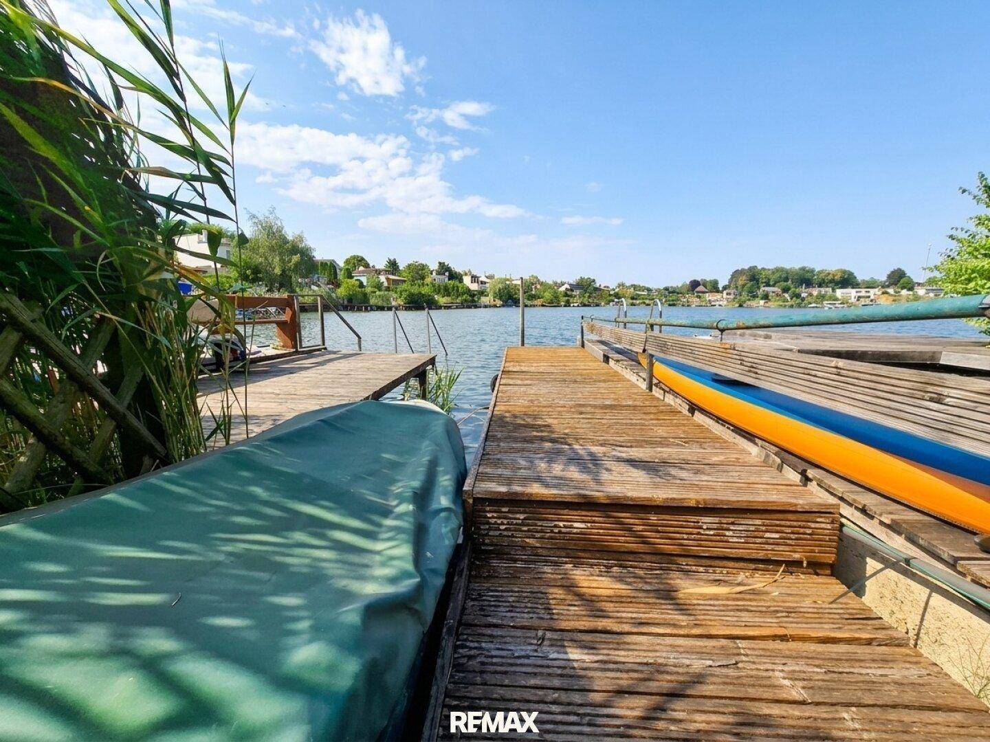 Holzsteg am Seeufer mit Booten, bietet direkten Zugang zum Wasser unter blauem Himmel.