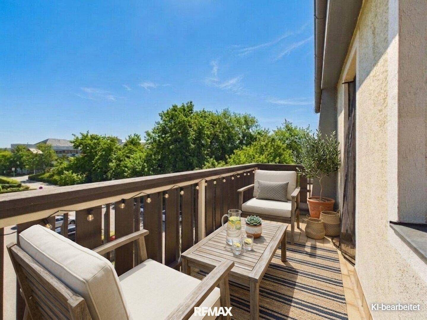 Heller Balkon mit bequemen Gartenmöbeln, Holztisch und Blick ins Grüne unter blauem Himmel.