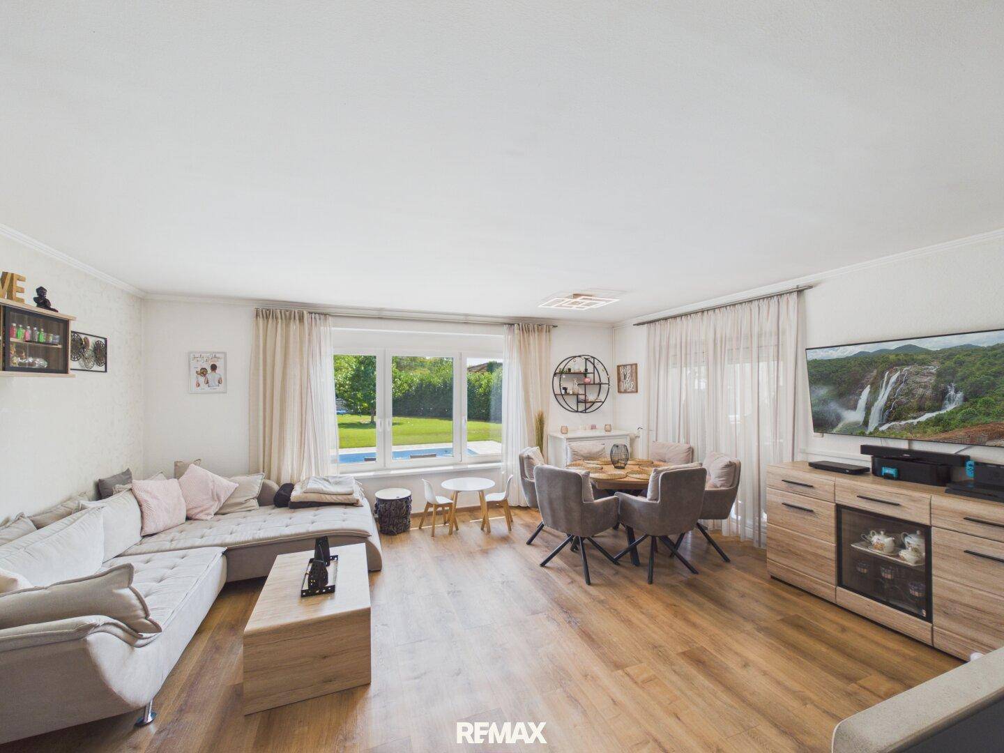 Gemütlicher Wohnbereich mit großem Sofa, Fernseher und Blick auf den Garten und Pool.