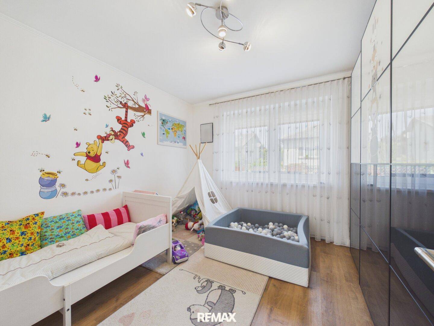 Kinderzimmer mit verspielter Wanddekoration, Bett und Spielbereich am Fenster.