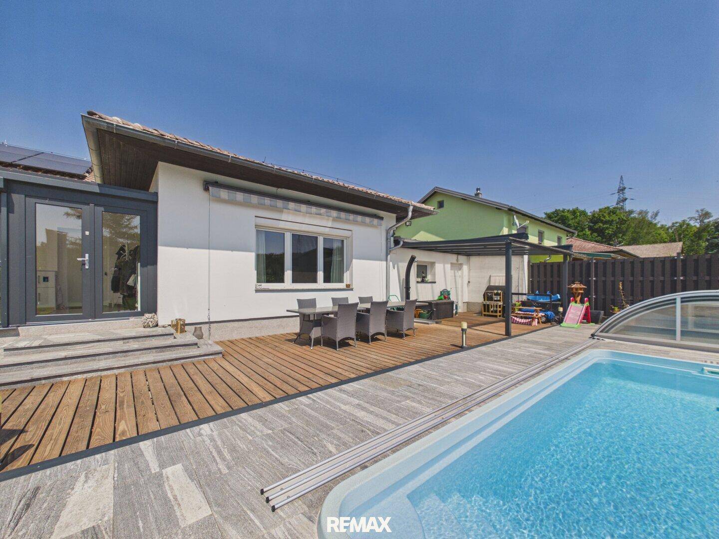 Terrasse mit Essbereich, Swimmingpool und Zugang zum Wintergarten, umgeben von Grün.