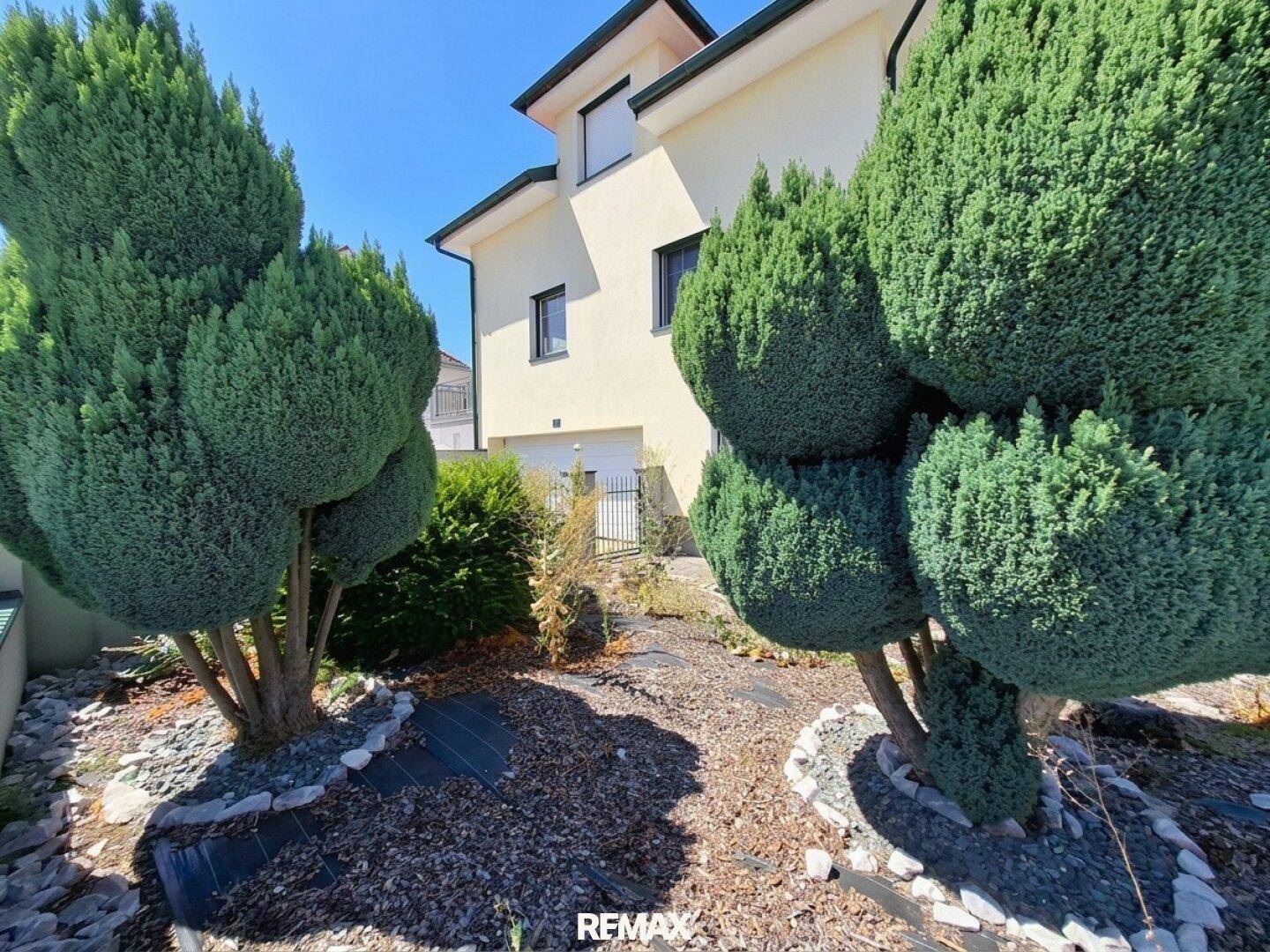 Gepflegter Gartenbereich mit Zierbäumen und Kiesbeeten, umgeben von viel Grün.