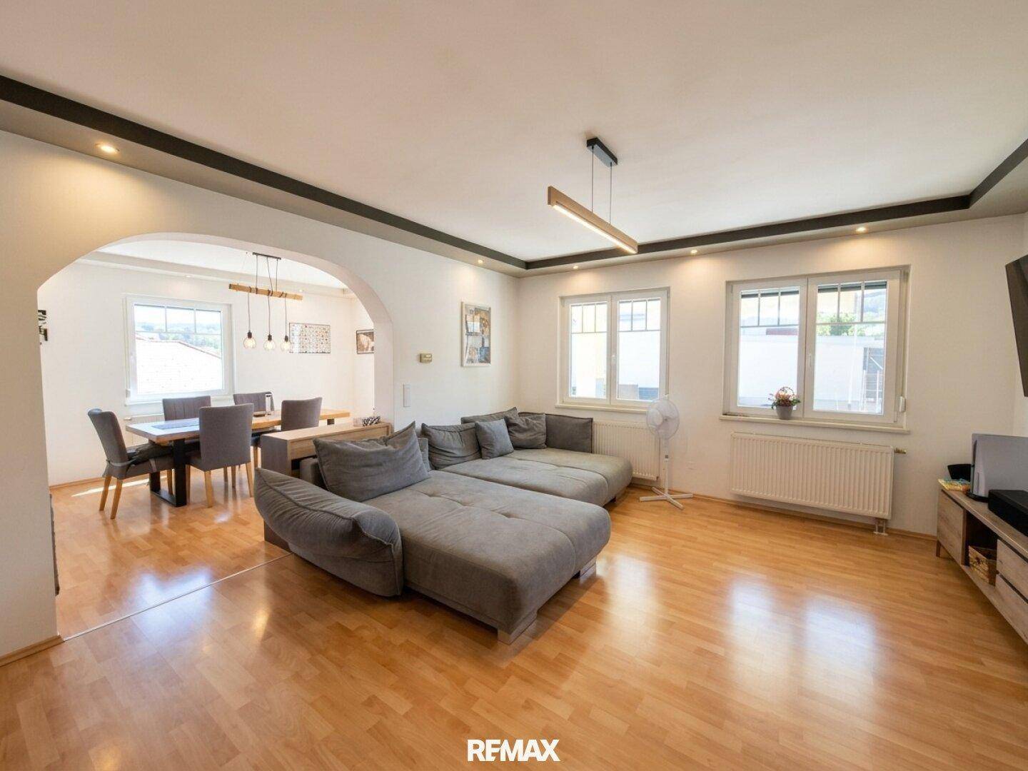 Geräumiger Wohn- und Essbereich mit Parkettboden, großem Sofa und viel Tageslicht.