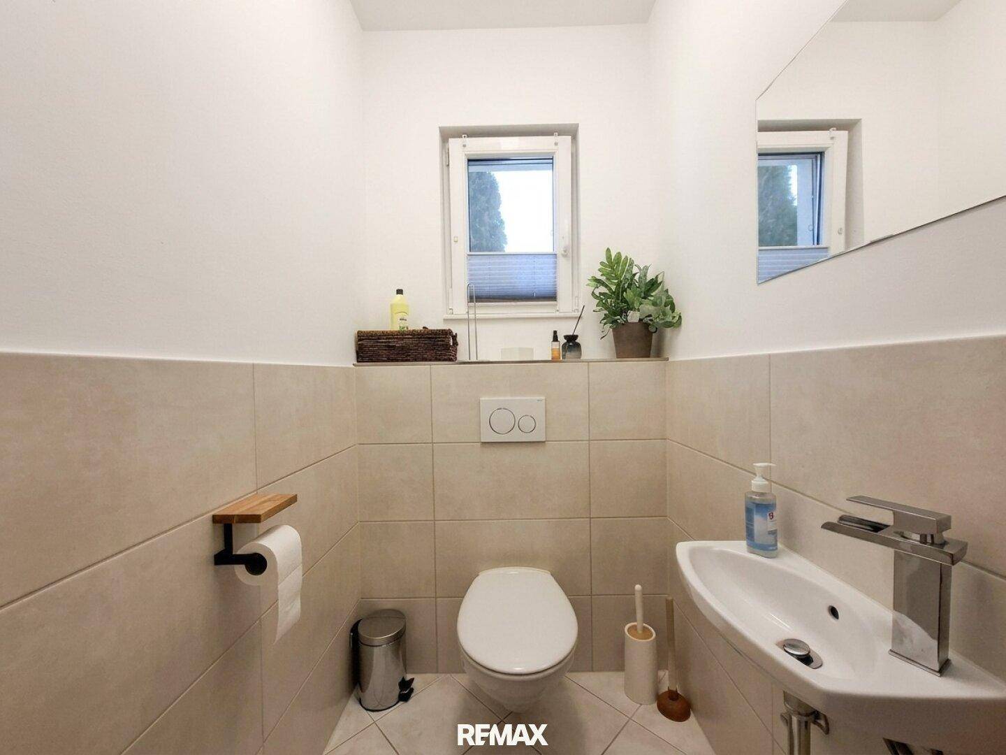 Separates Gäste-WC mit wandhängendem WC, kleinem Waschbecken und Fenster.