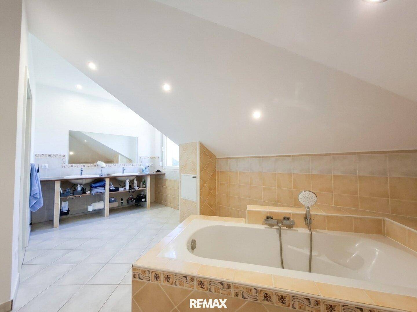 Großes Dachgeschoss-Badezimmer mit Doppelwaschbecken, Badewanne und hellen Fliesen.