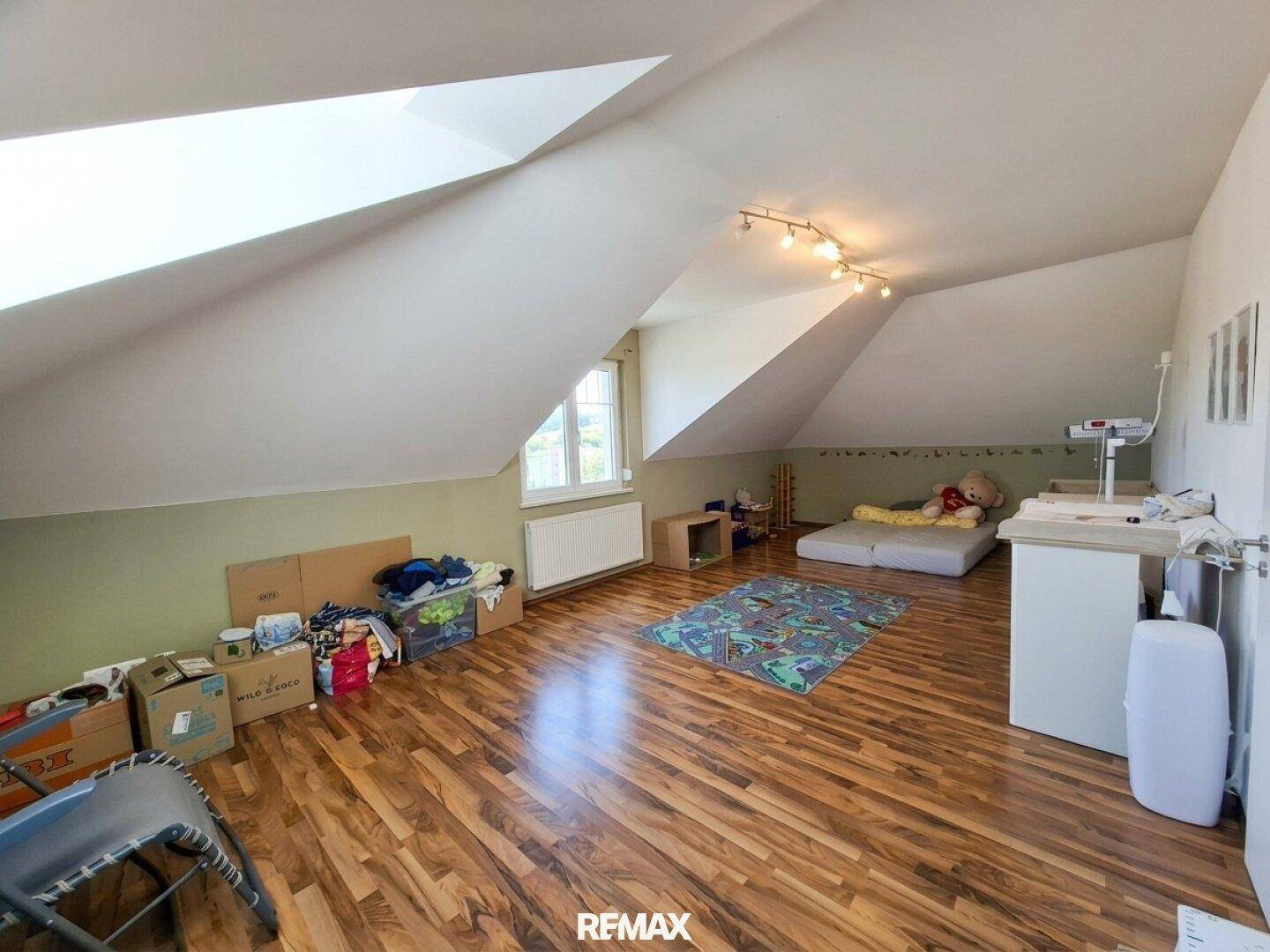 Helles Schlafzimmer im Dachgeschoss mit Holzboden, Dachschrägen und Fenster.