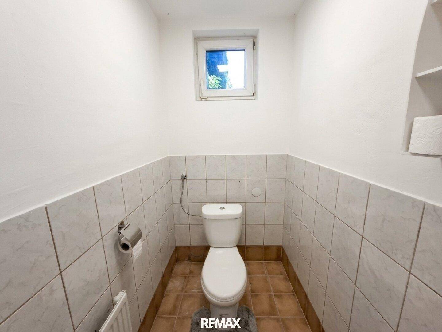 Kleines Gäste-WC mit Fenster und gefliesten Wänden, funktional und hell gestaltet.