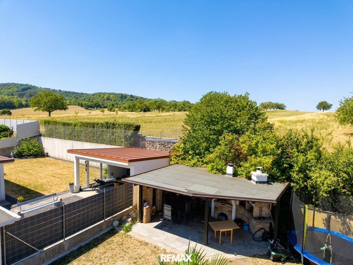 Großer Gartenbereich mit überdachtem Grillplatz, Trampolin und weitem Blick ins Grüne.