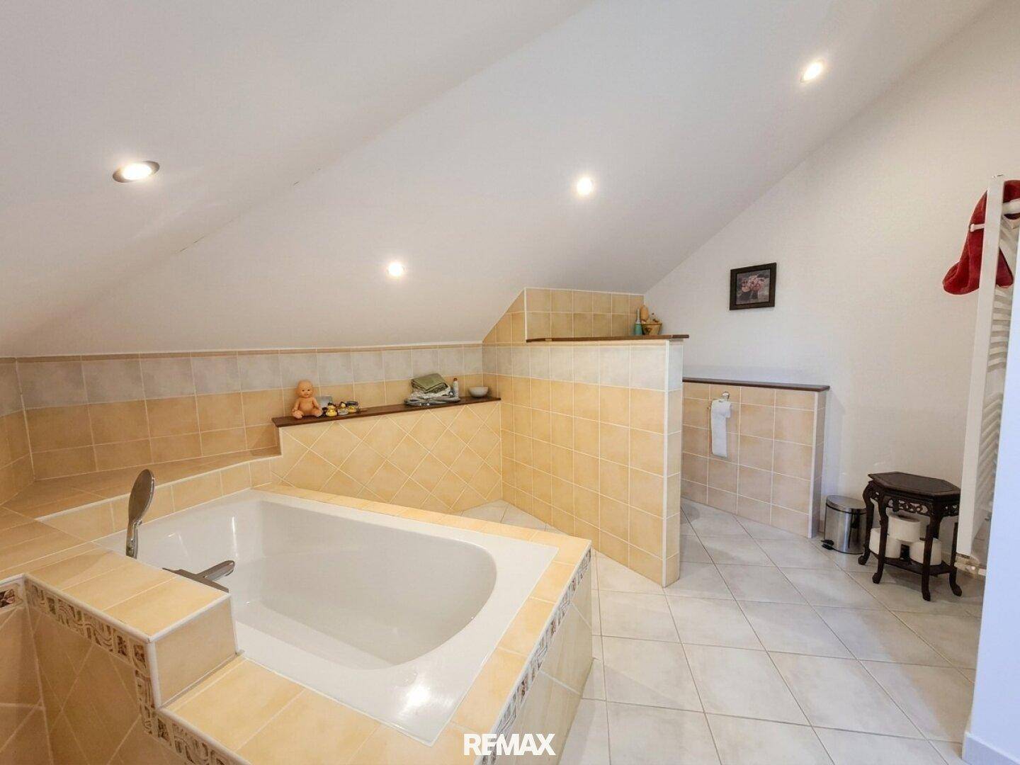Geräumiges Badezimmer im Dachgeschoss mit großer Badewanne und beigefarbenen Fliesen.
