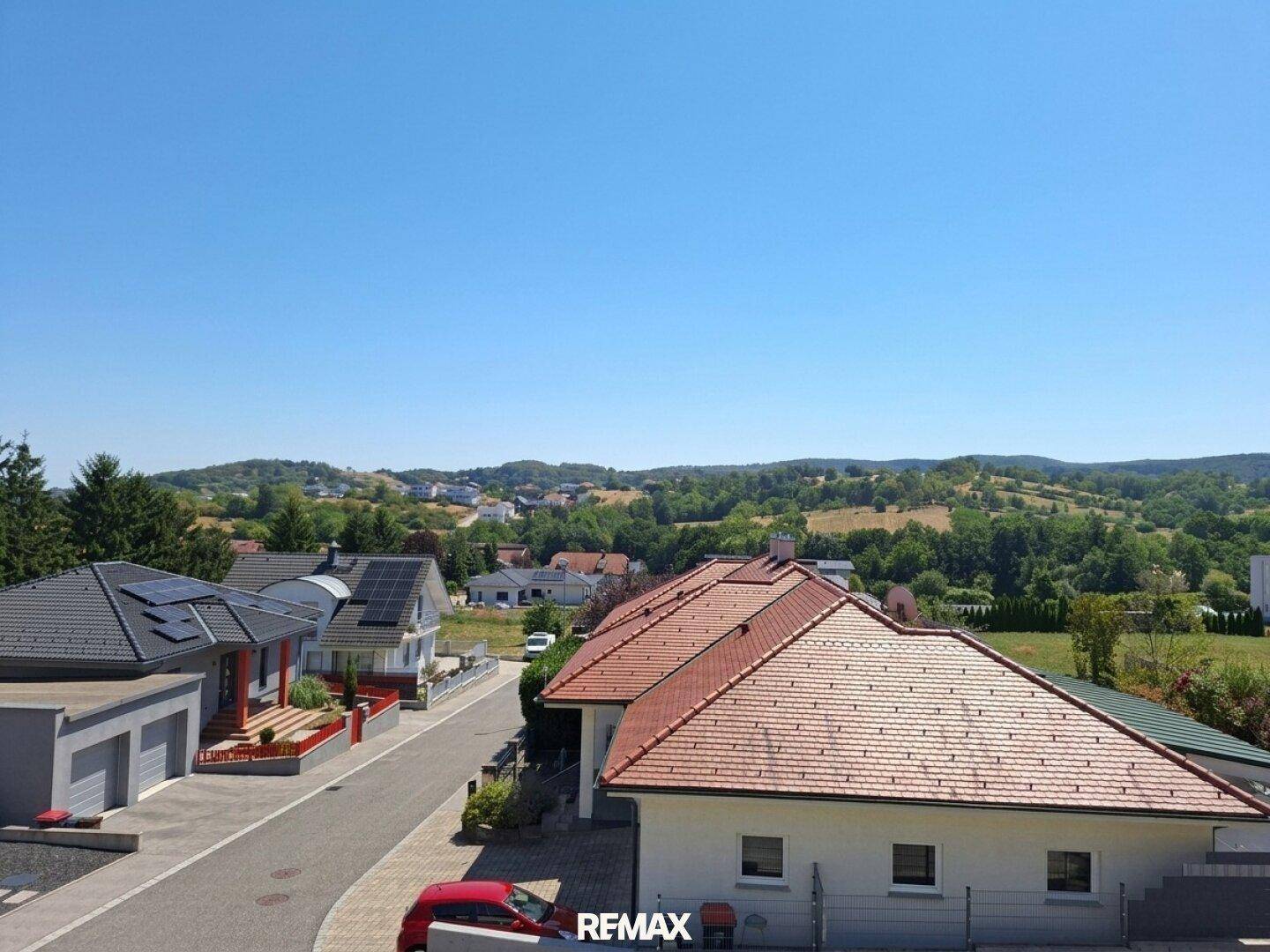 Weitläufiger Blick über die Nachbarschaft mit Häusern und grünen Hügeln im Hintergrund.