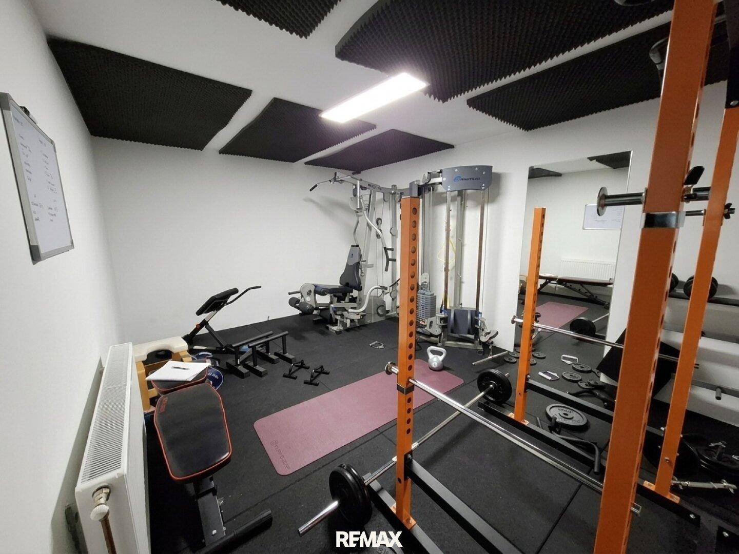 Gut ausgestatteter Fitnessraum mit Gewichten, Spiegeln und schallabsorbierenden Deckenplatten.