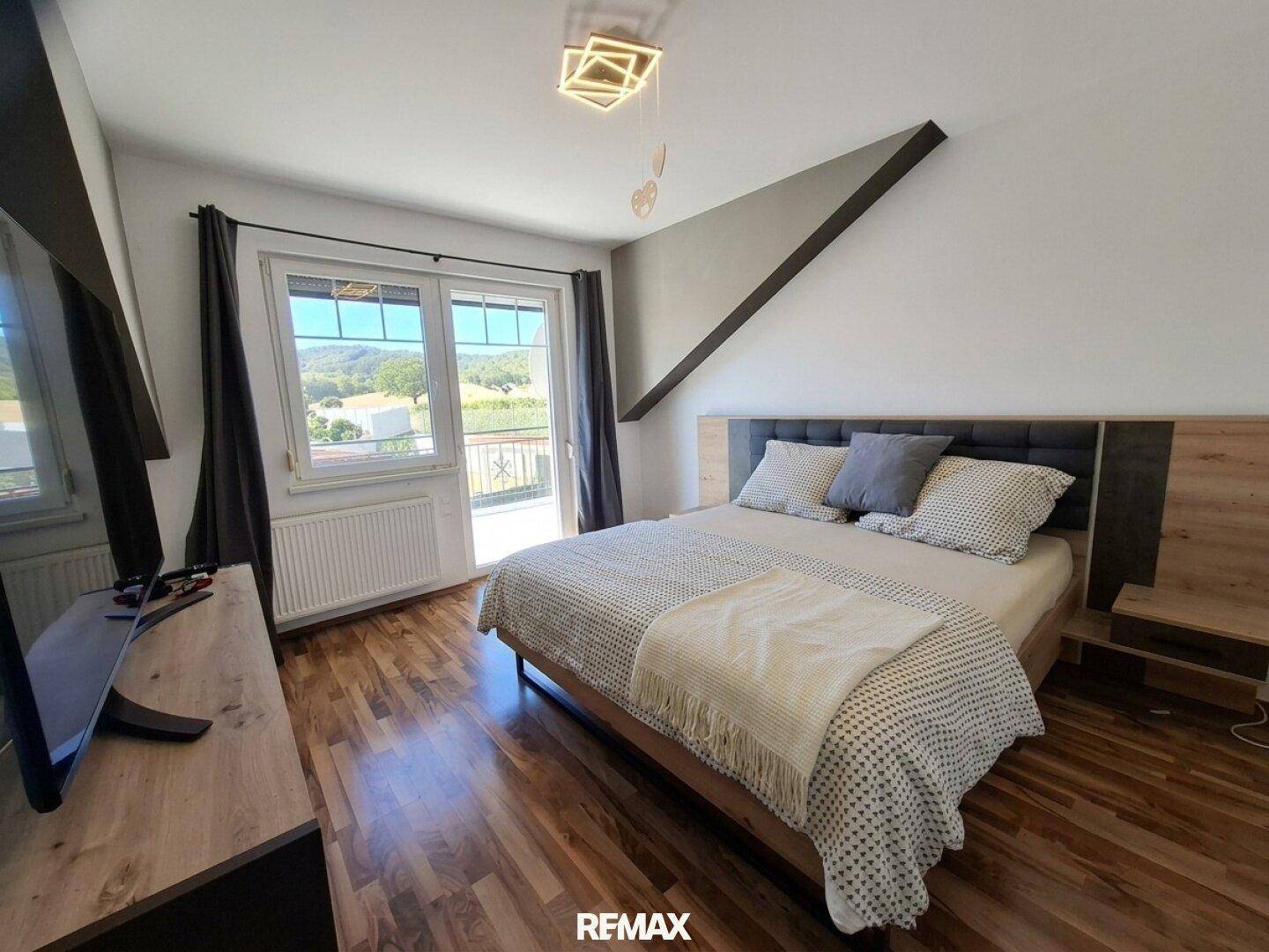 Helles Schlafzimmer mit Holzboden, Zugang zum Balkon und weitem Blick ins Grüne.