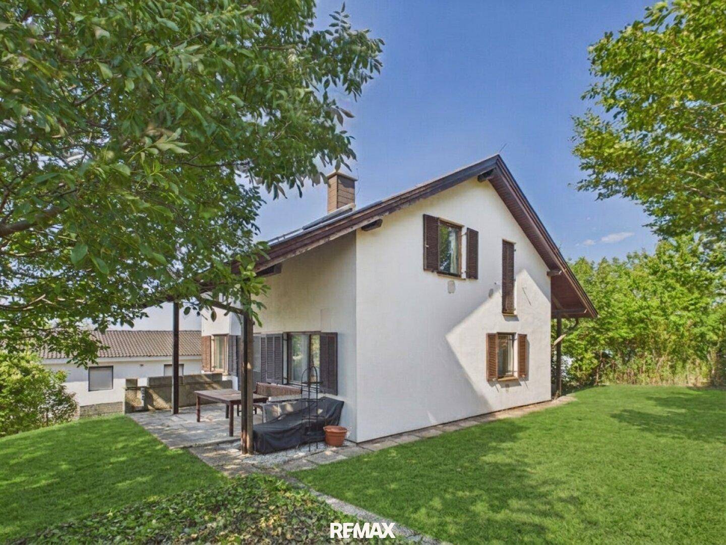 Gepflegter Gartenbereich mit Rasenfläche und einer kleinen überdachten Terrasse am Haus.