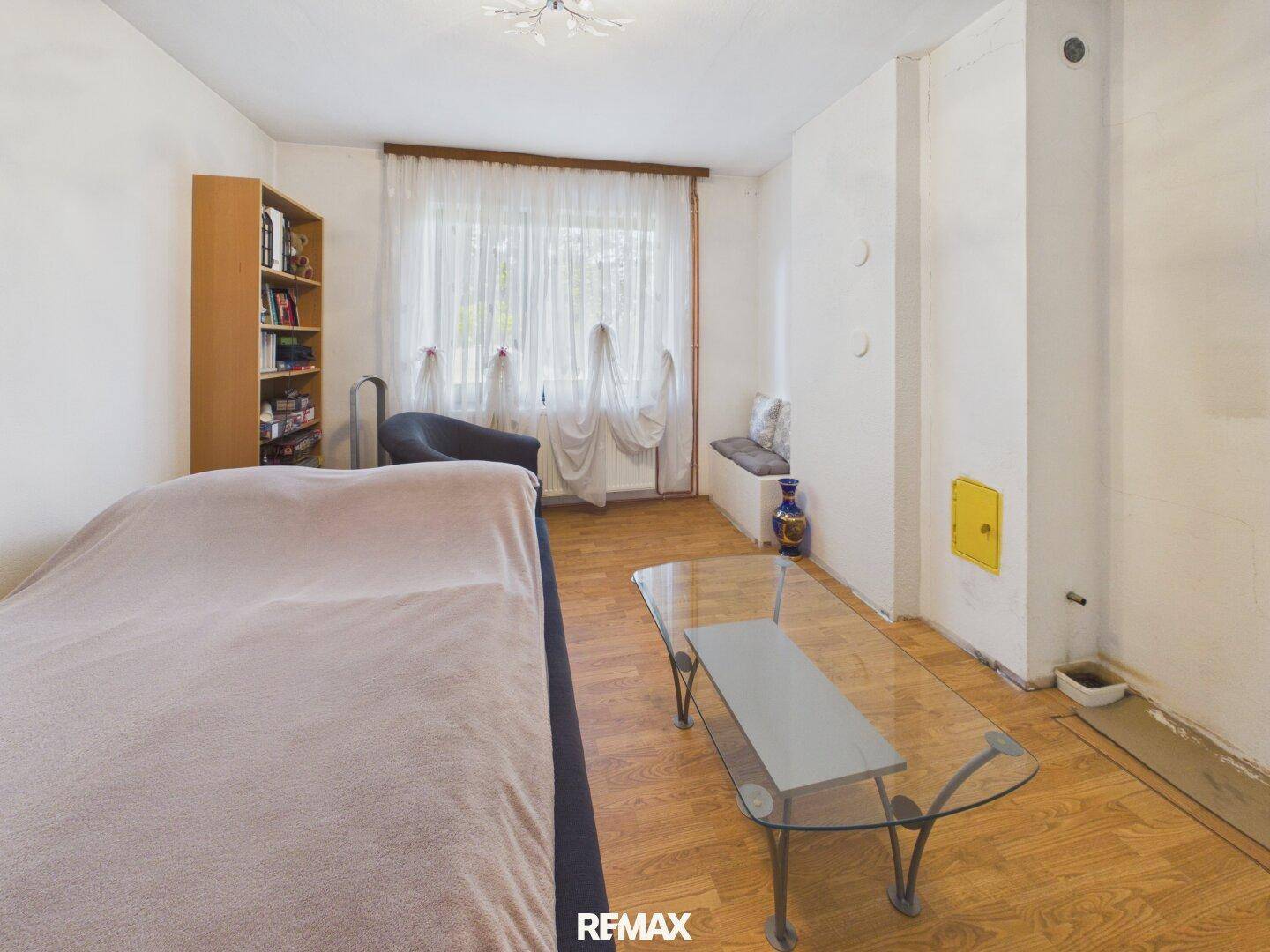 Schlafzimmer mit Holzboden, großem Fenster und einem Kachelofen an der Wand.