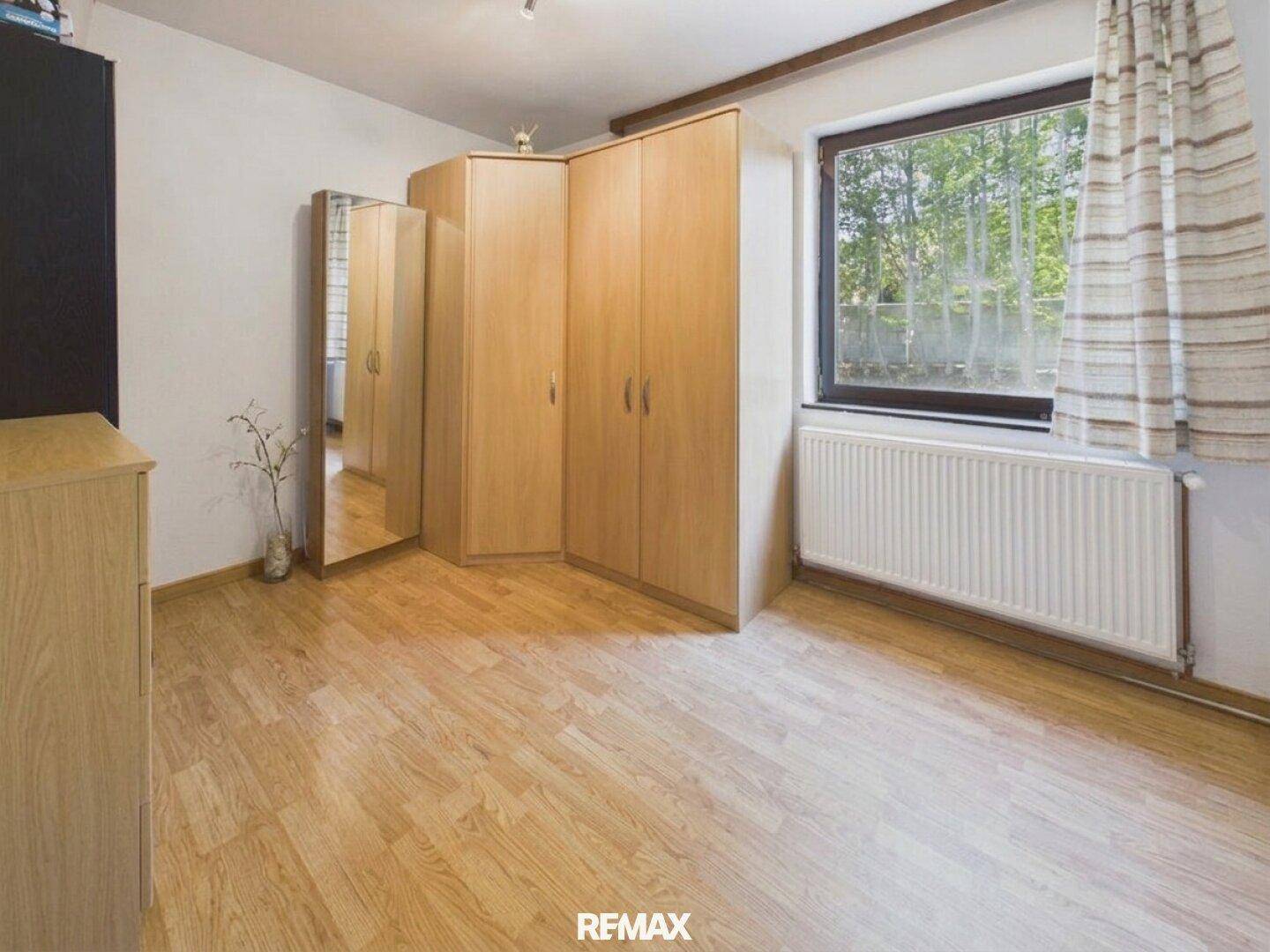 Schlafzimmer mit Laminatboden, großem Fenster und Einbauschränken aus hellem Holz.