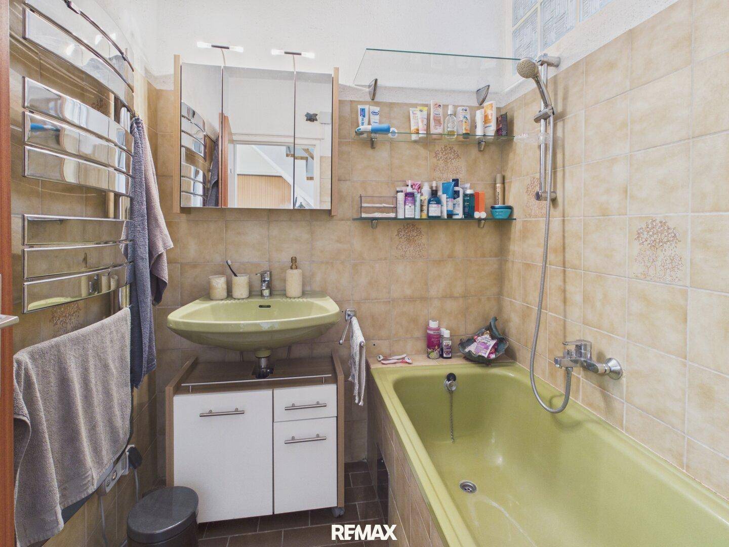 Badezimmer mit beigefarbenen Fliesen, Badewanne und beheiztem Handtuchhalter.