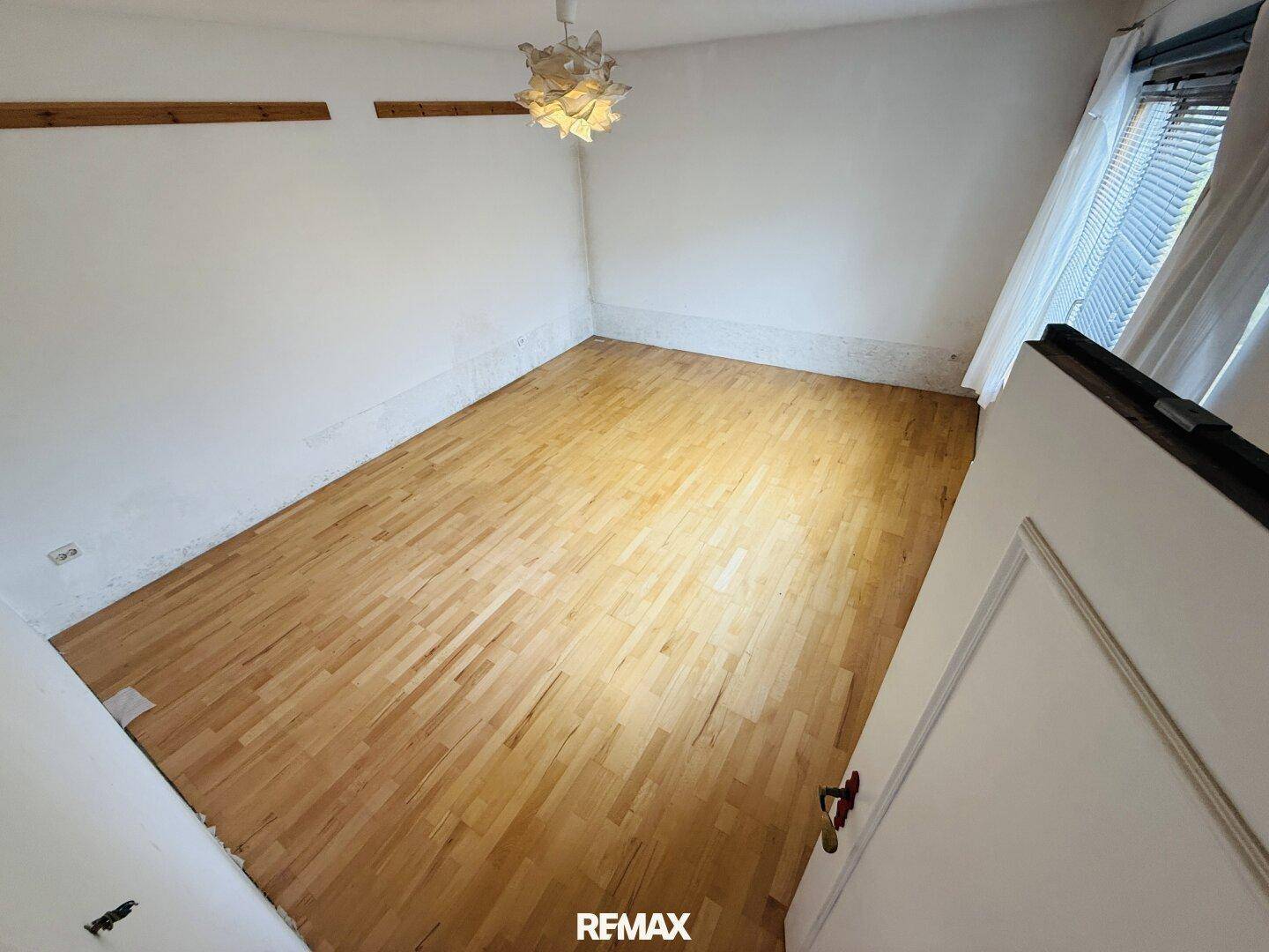 Leerer Raum mit hellem Holzfußboden und einem Fenster, bereit zur individuellen Gestaltung.