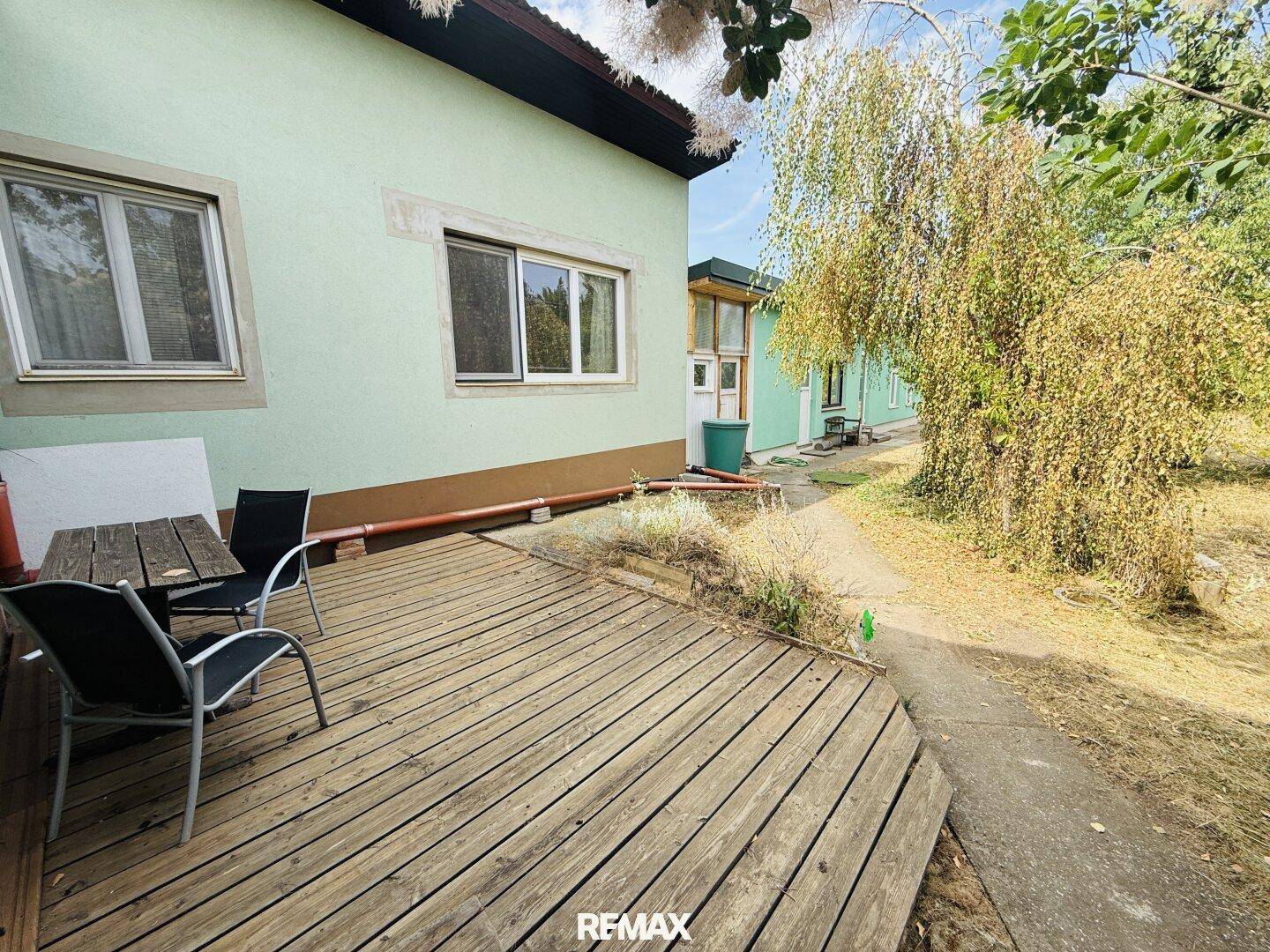 Detailansicht der Holzterrasse mit Gartenmöbeln direkt am Haus, umgeben von Grün.