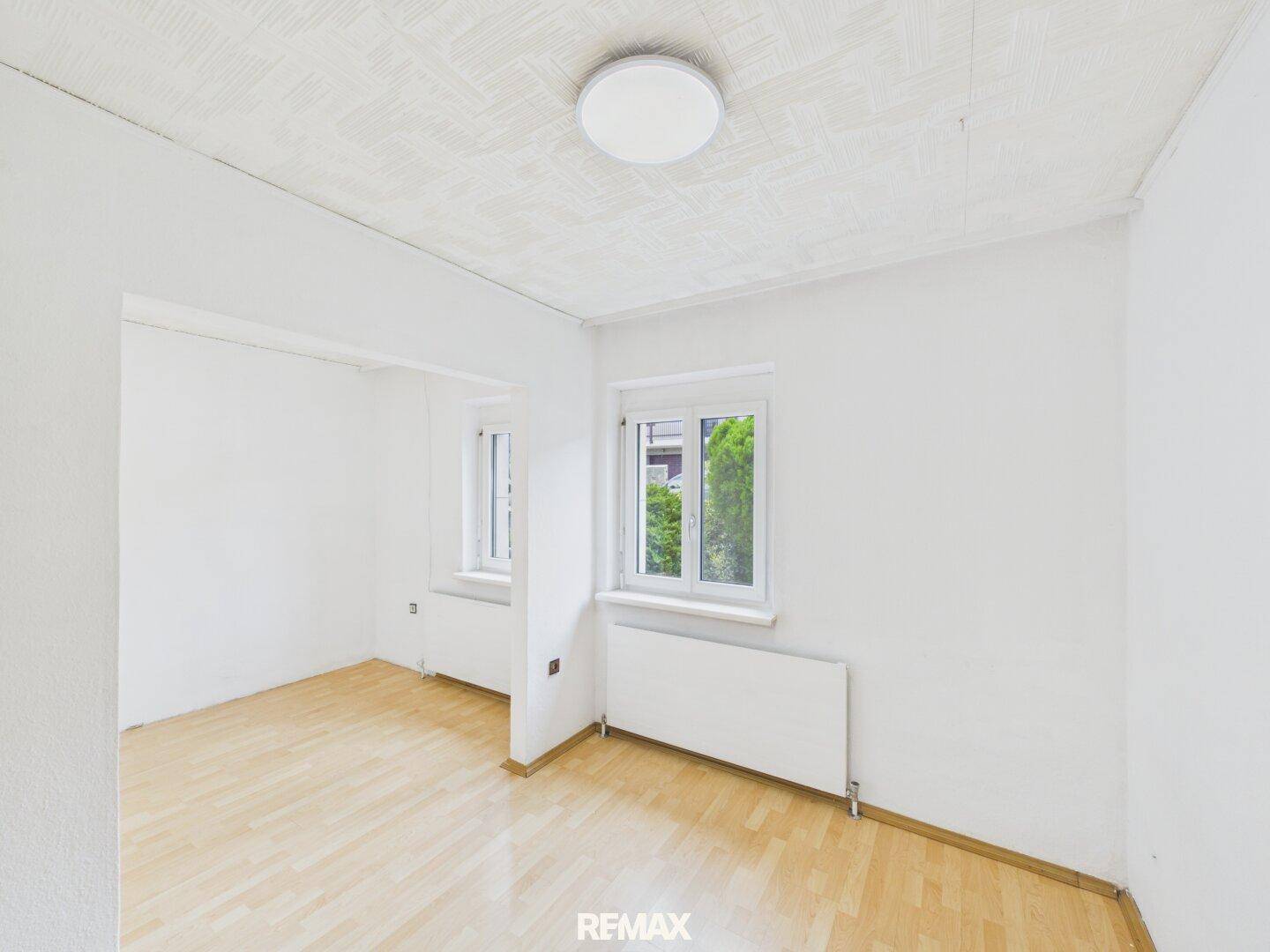 Schlafzimmer mit Parkettboden, zwei Fenstern und Heizkörpern, hell und funktional.