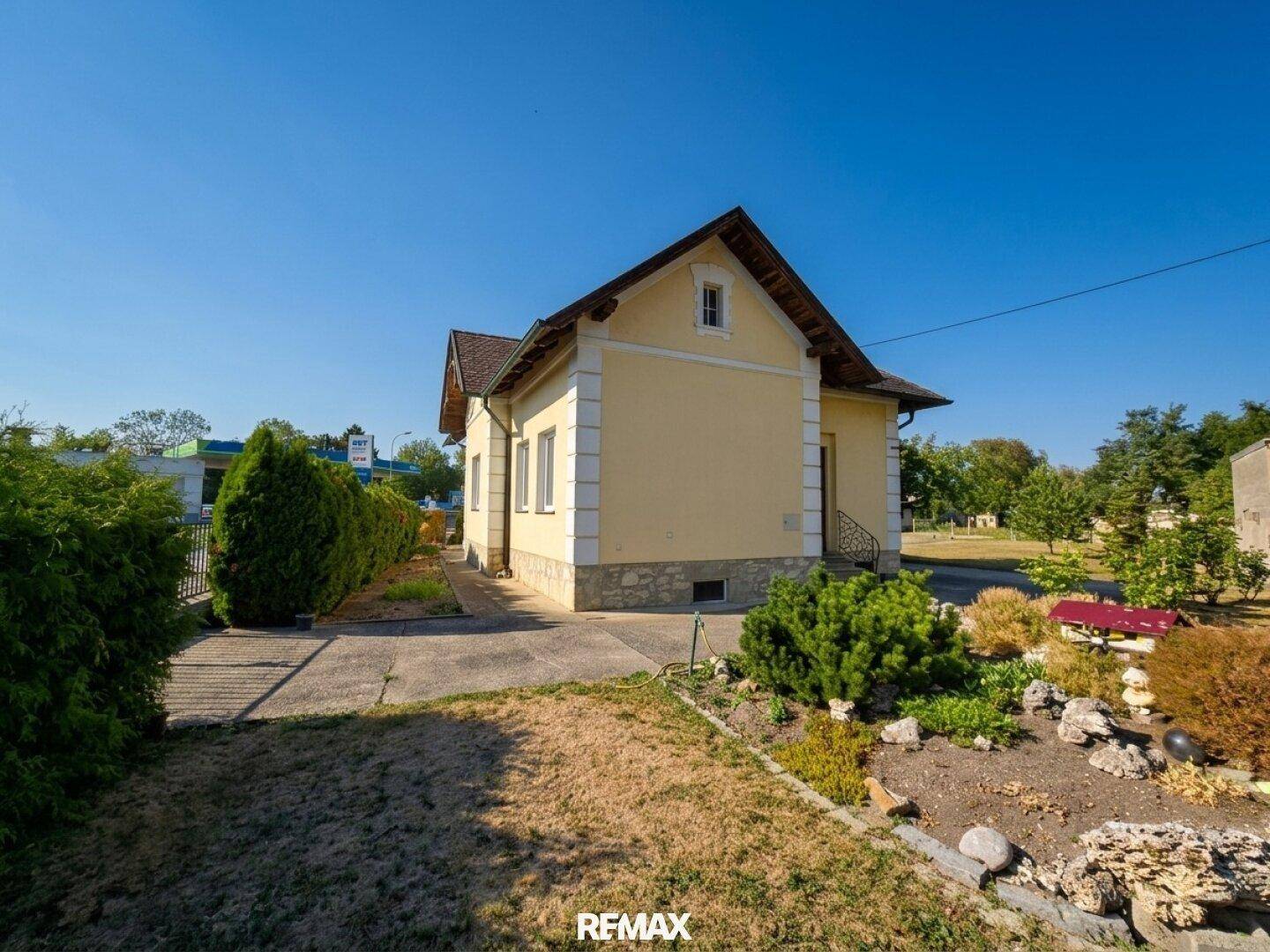 Gelbes Einfamilienhaus mit Satteldach und gepflegtem Vorgarten unter blauem Himmel.