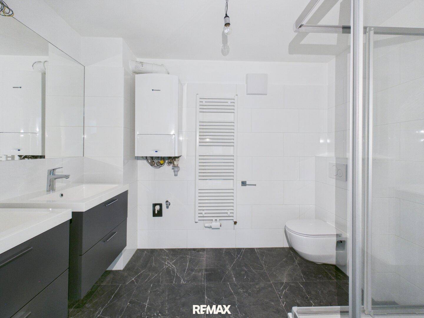 Modernes Badezimmer mit dunklen Fliesen, Dusche, Doppelwaschbecken und Handtuchheizkörper.