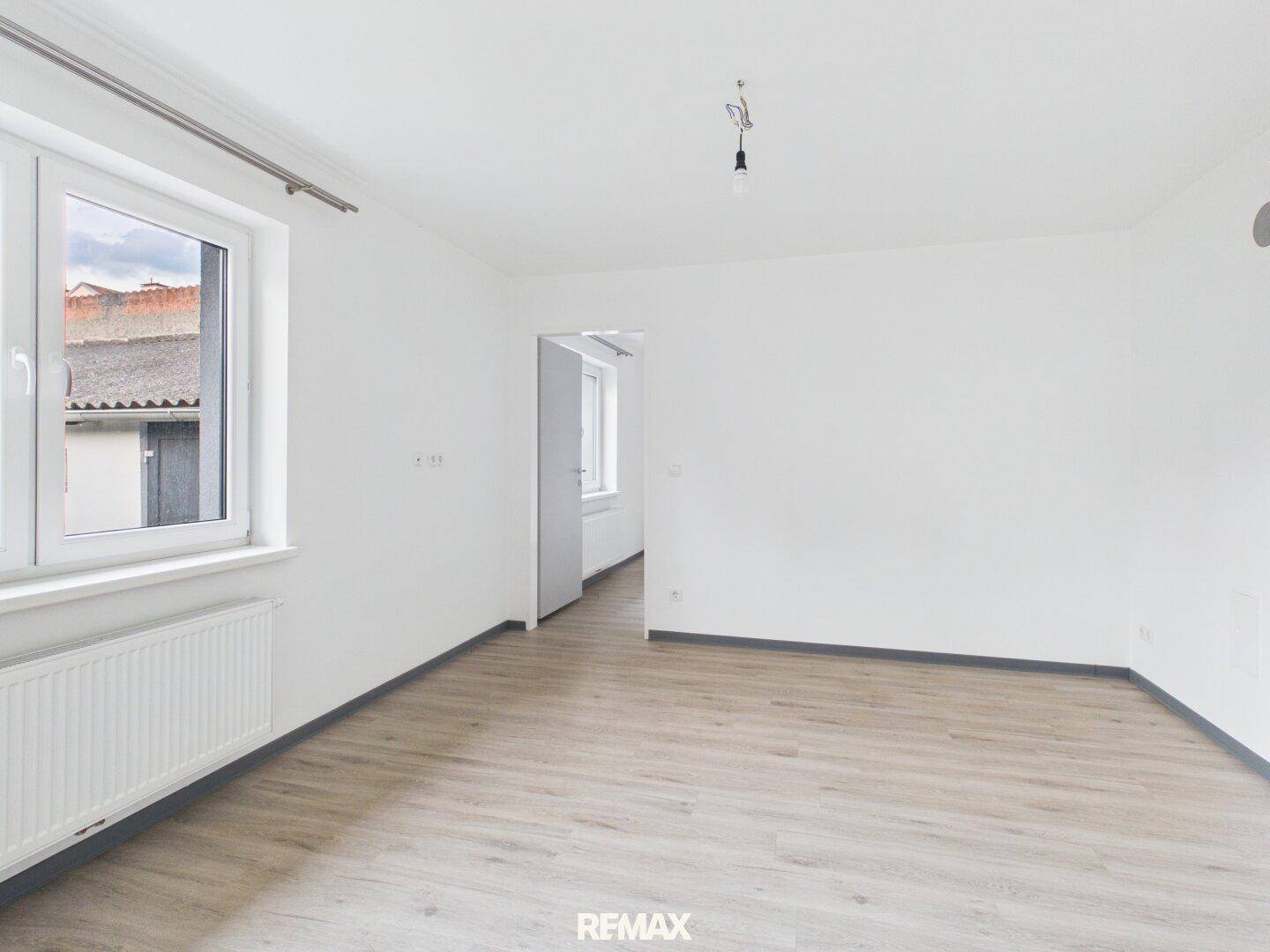 Lichtdurchfluteter Wohnraum mit neuem Laminatboden und großem Fenster.
