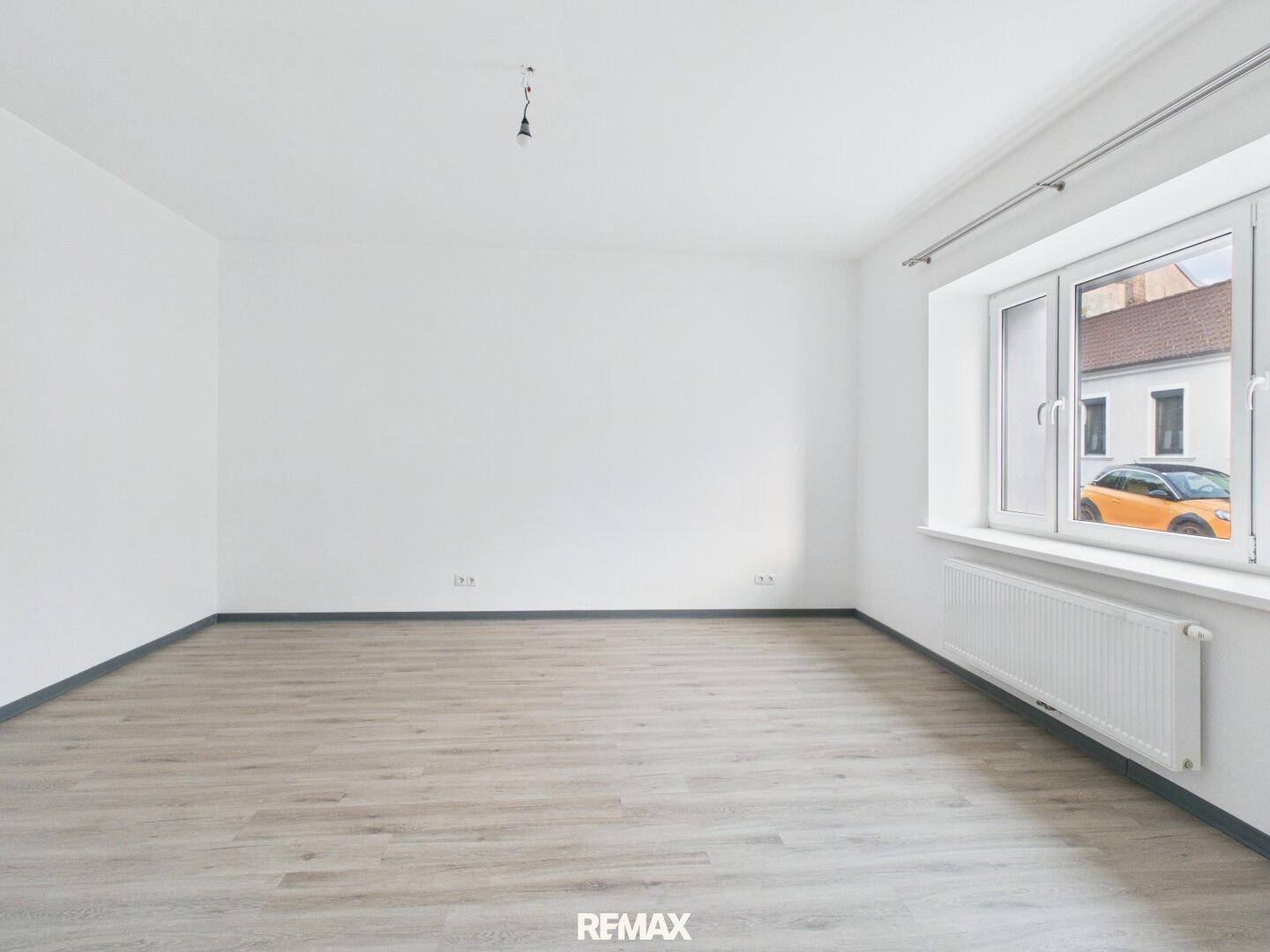 Geräumiger, heller Raum mit Laminatboden und großem Fenster zur Straßenseite.