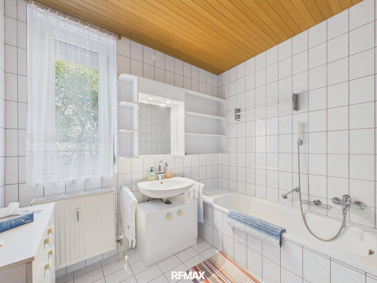 Gefliestes Badezimmer mit Badewanne, Waschbecken und Fenster für Tageslicht.