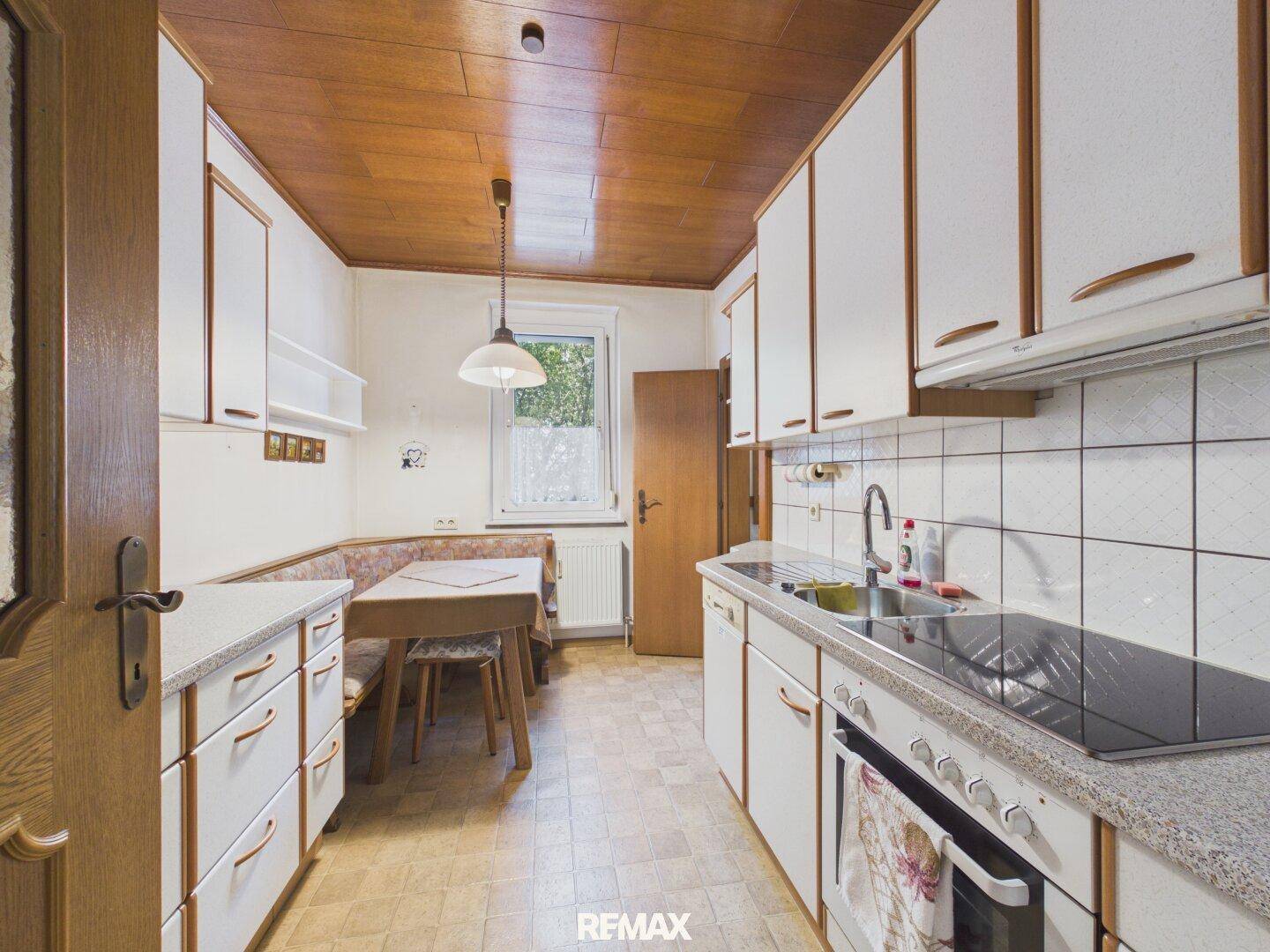 Funktionale Küche mit weißen Schränken, Essbereich und einer Holzpaneeldecke.
