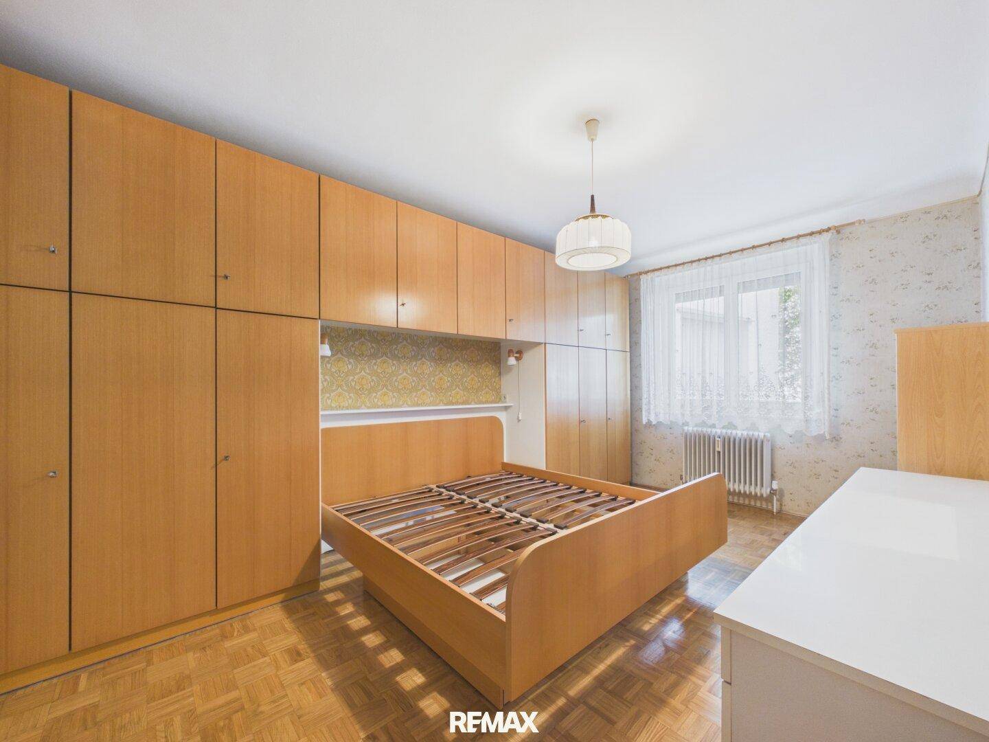 Schlafzimmer mit Einbauschränken, Parkettboden und einem Bettgestell aus hellem Holz.
