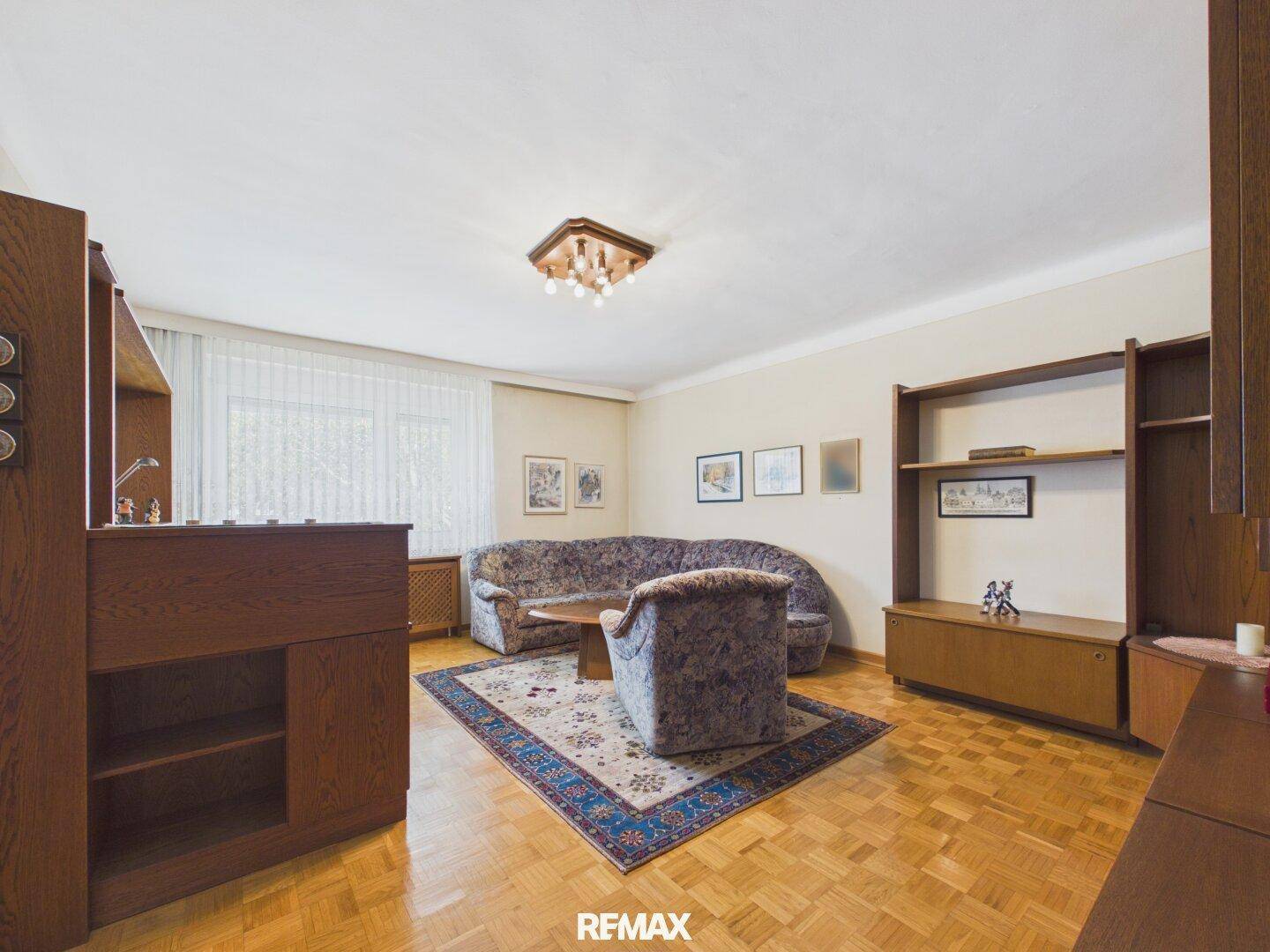 Gemütliches Wohnzimmer mit Parkettboden, einem Sofa und Sessel sowie einer Holzpaneeldecke.