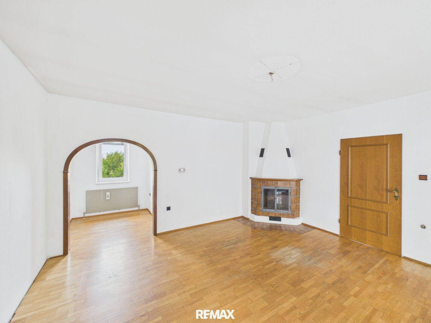 Geräumiges Wohnzimmer mit Parkettboden, Kamin und Rundbogen zum Nebenraum.