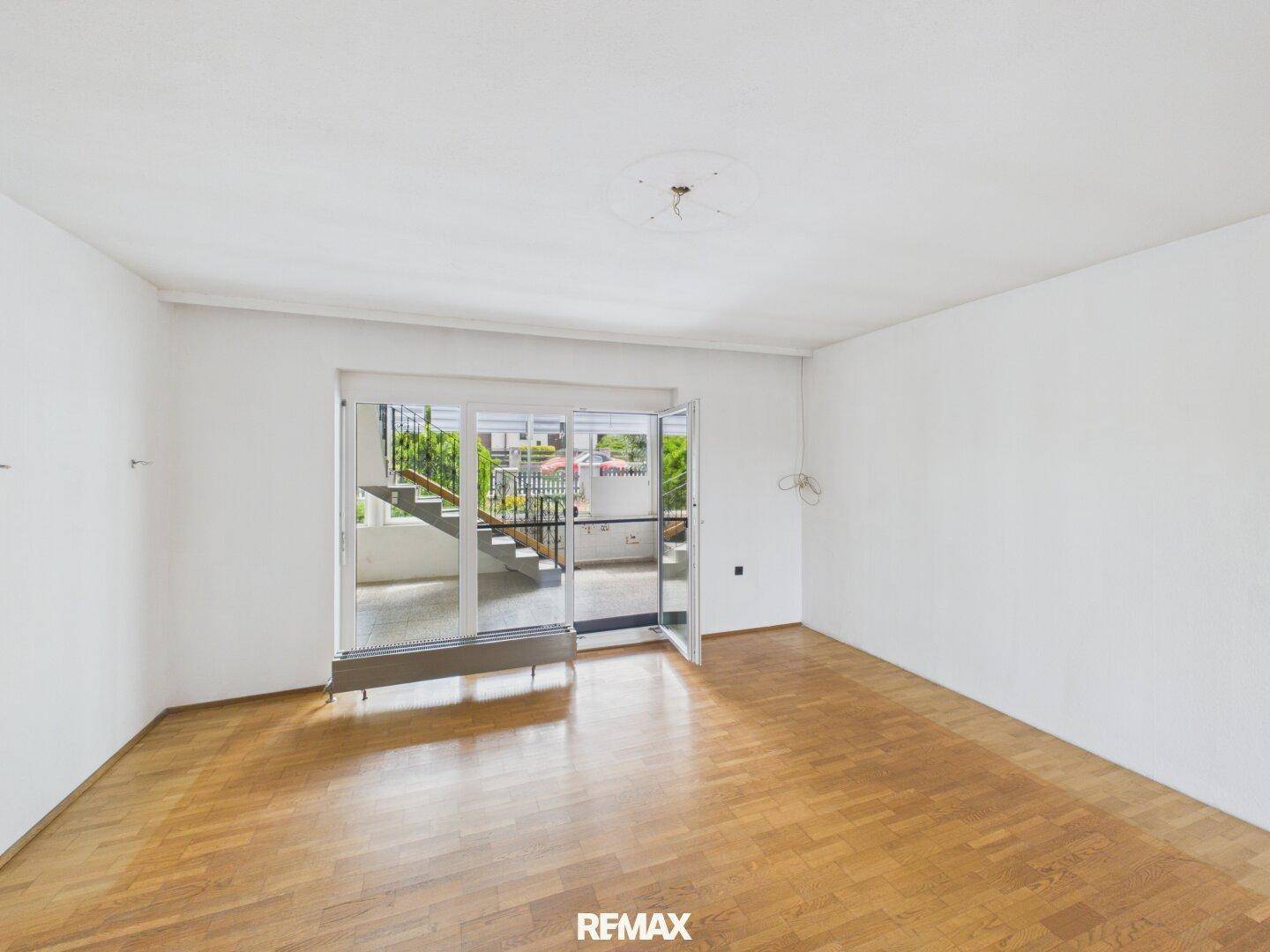 Helles Wohnzimmer mit Parkettboden und Zugang zu einem Außenbereich mit Treppe.