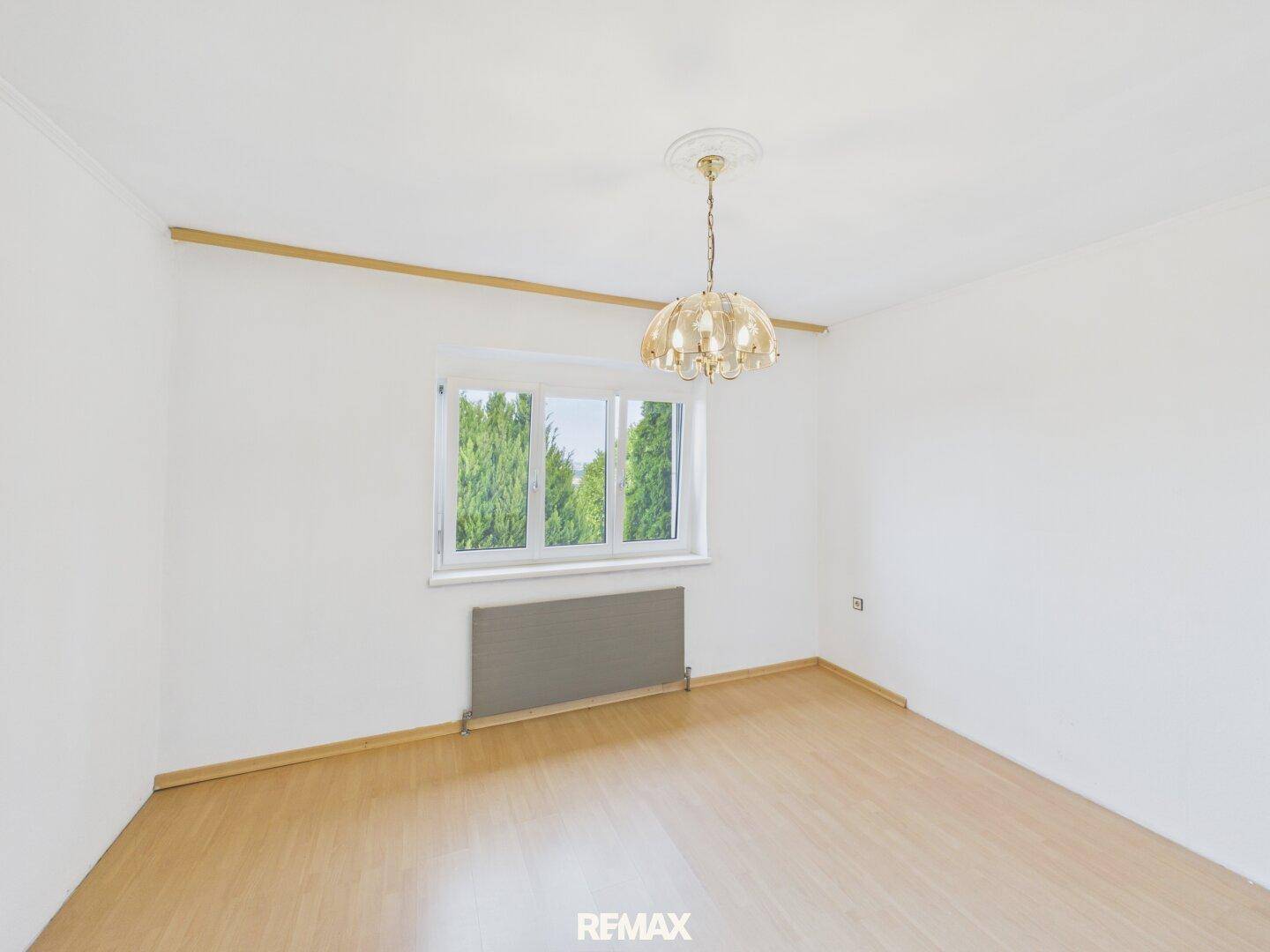 Helles Schlafzimmer mit Parkettboden, großem Fenster und klassischer Deckenleuchte.
