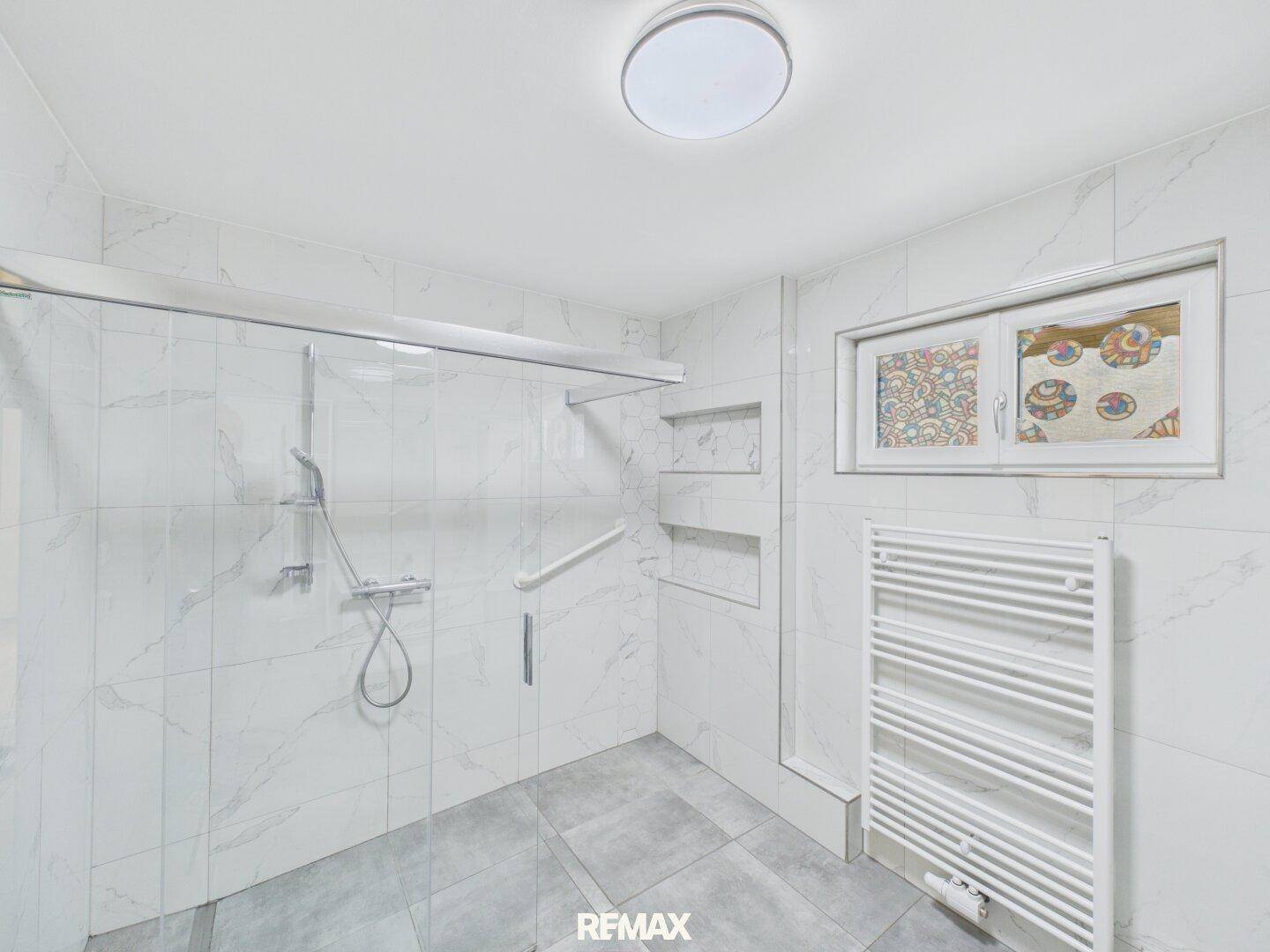 Modernes Badezimmer mit großer begehbarer Dusche, weißen Fliesen und Handtuchheizkörper.