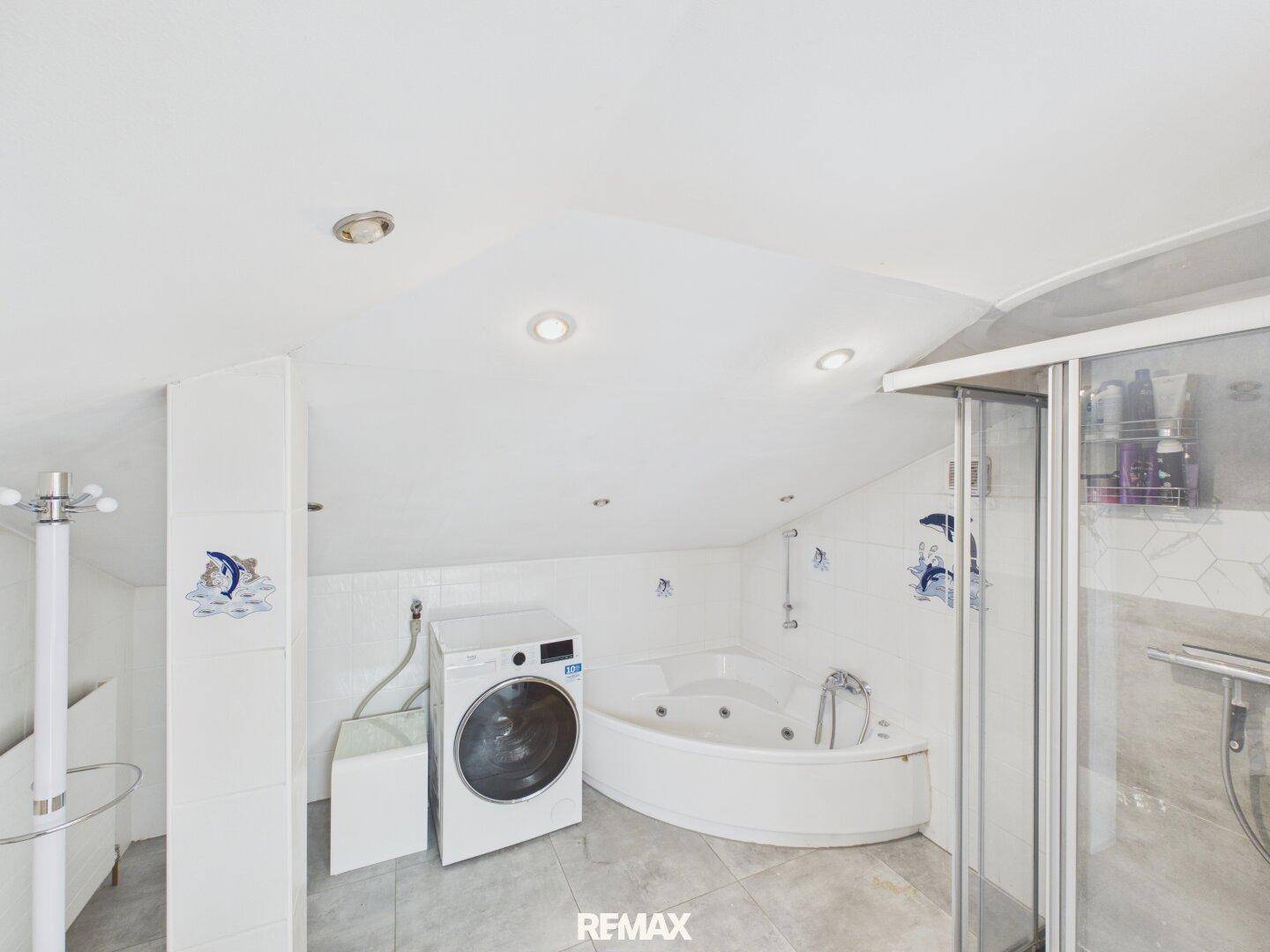 Badezimmer im Dachgeschoss mit Eckbadewanne, Dusche und Waschmaschine.