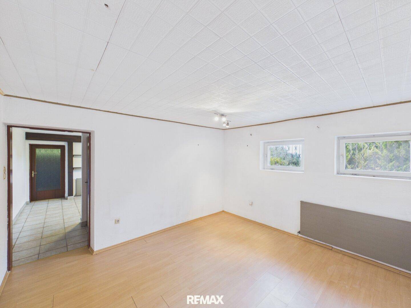Helles Zimmer im Untergeschoss mit Laminatboden und zwei Fenstern.