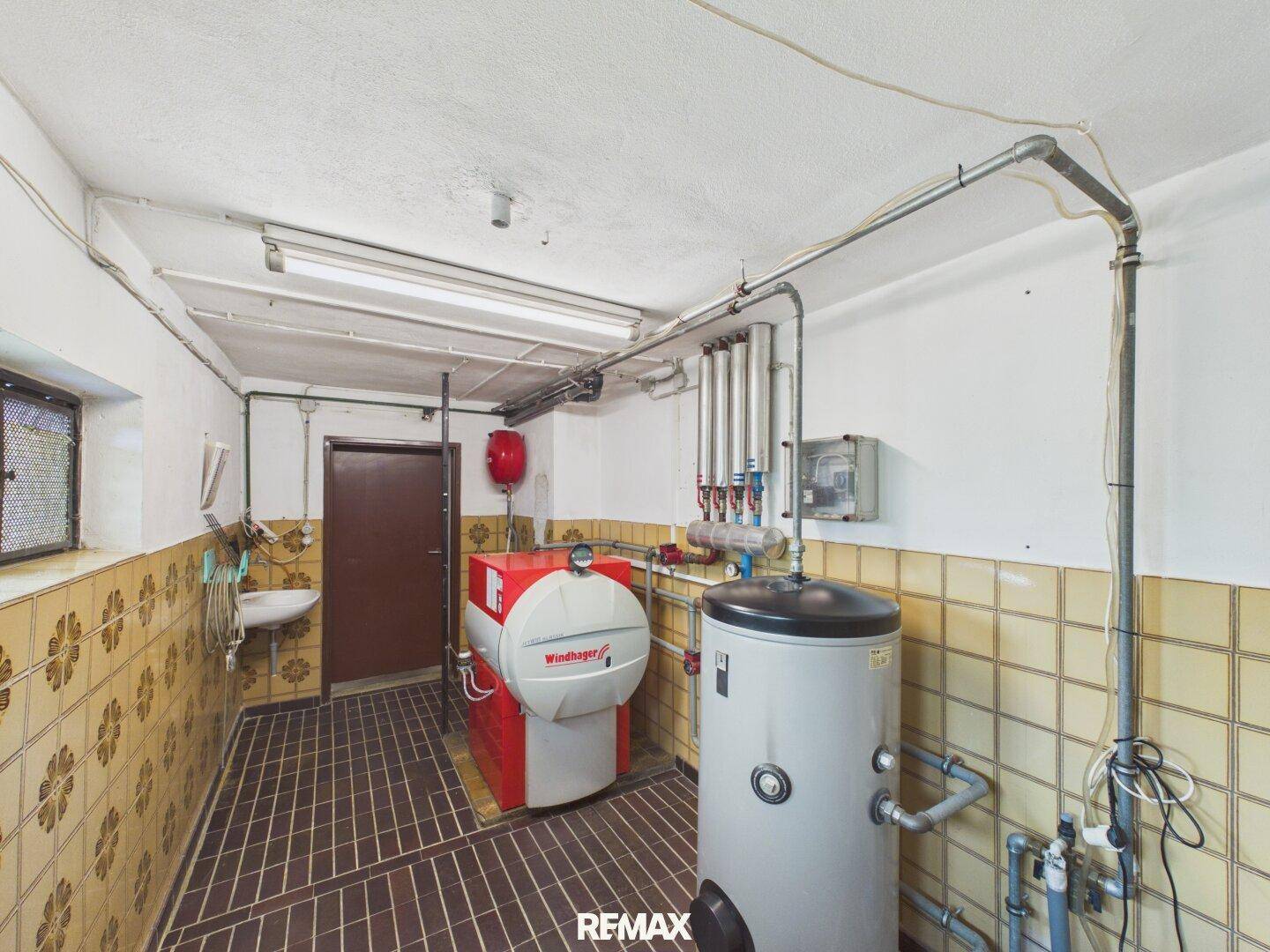 Heizraum mit Kessel, Warmwasserspeicher und alten Fliesen an den Wänden.