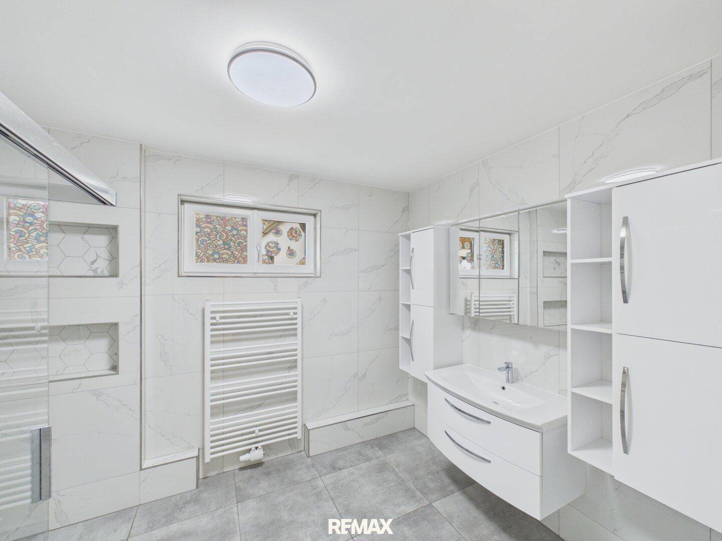 Modernes Badezimmer mit Waschtisch, Spiegelschrank, begehbarer Dusche und weißen Fliesen.