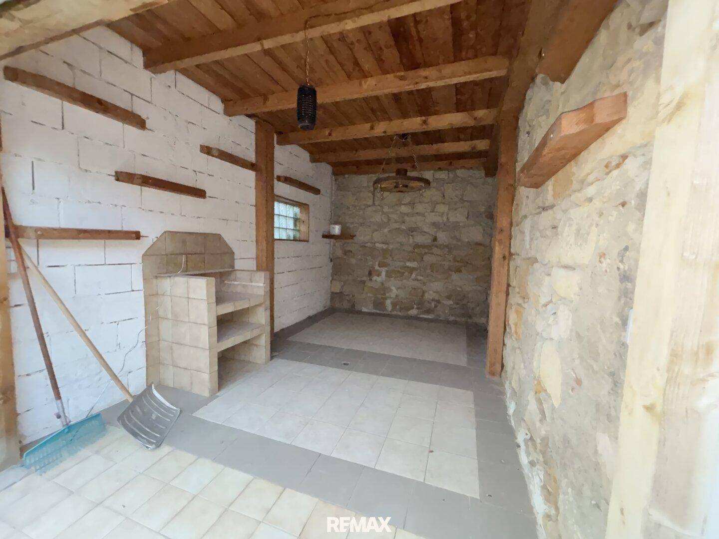 Rustikaler Abstellraum mit gefliestem Boden, Holzbalken und gemauerter Arbeitsfläche.