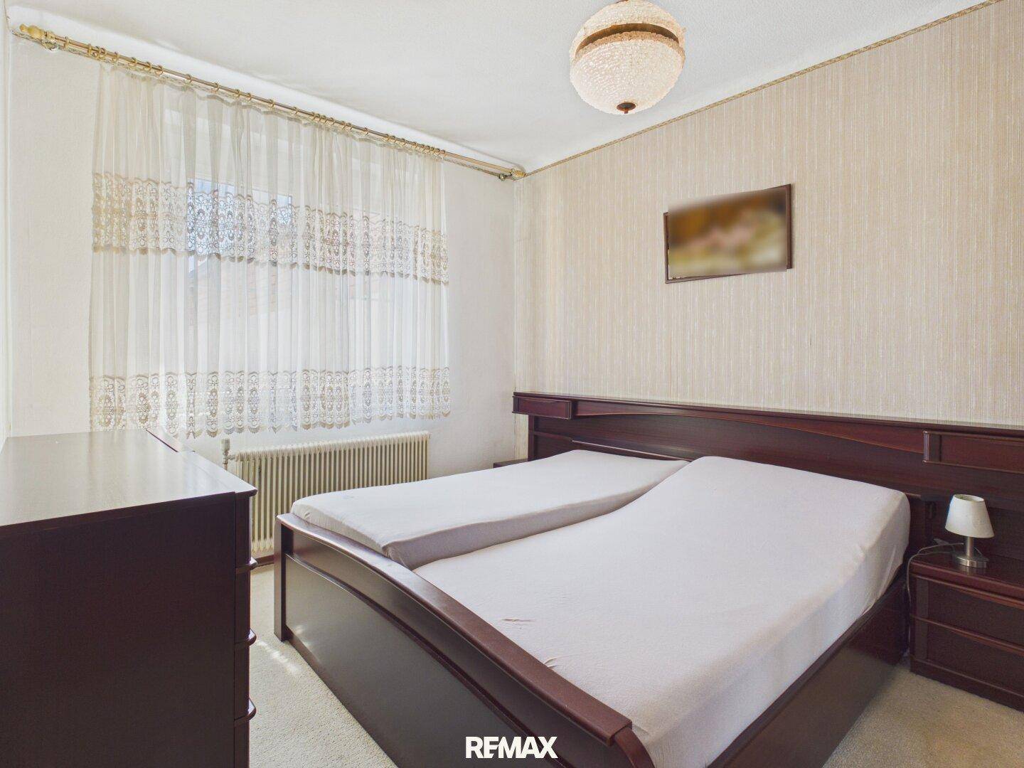 Schlafzimmer mit dunklem Holzdoppelbett, gemusterter Tapete und Teppichboden.