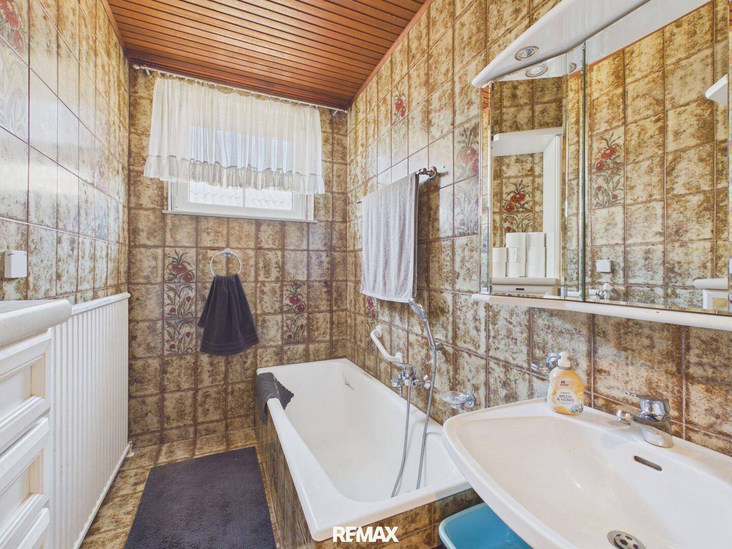 Badezimmer mit braunen Fliesen, Badewanne, Waschbecken und Spiegelschrank.
