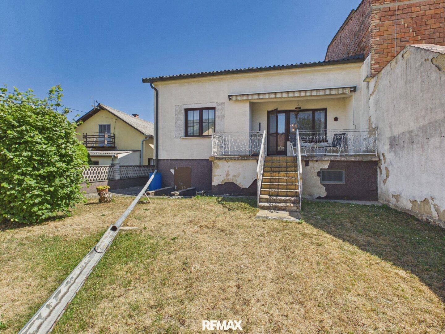 Hinteransicht des Hauses mit Terrasse, Treppe zum Garten und Rasenfläche.