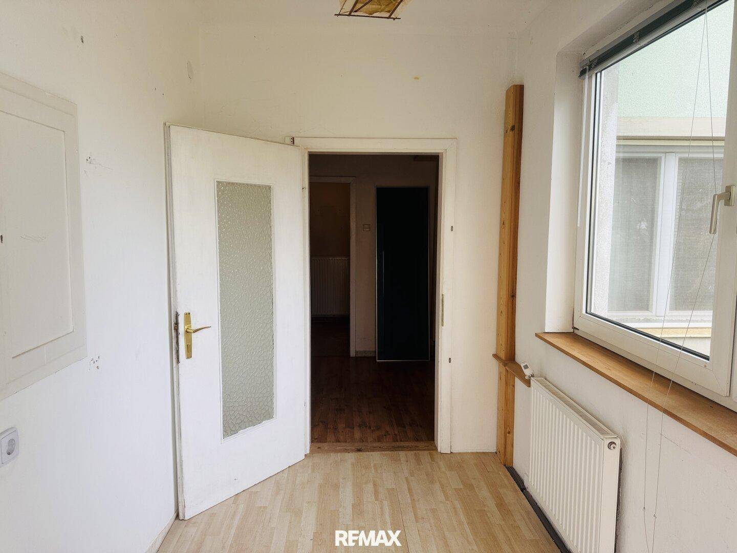 Heller Flur oder Vorraum mit Fenster, Heizkörper und einer Tür, die zu einem weiteren Raum führt.
