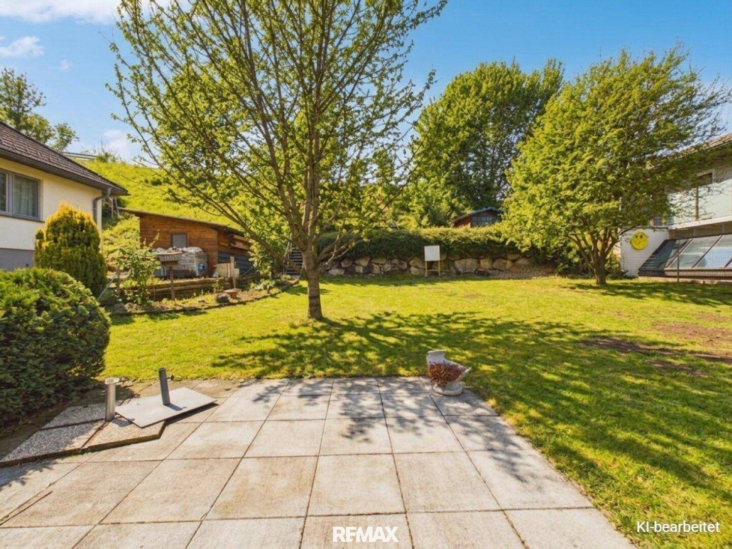 Gepflasterte Terrasse im Gartenbereich mit Blick auf Bäume und eine grüne Hügellandschaft.