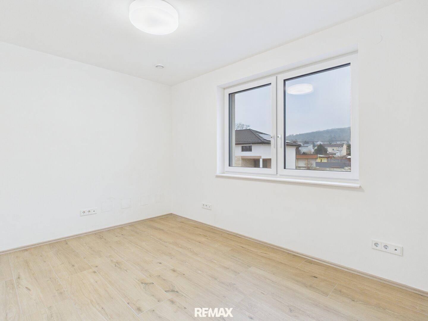 Unmöbliertes Schlafzimmer mit Laminatboden, großen Fenstern und Blick auf die Umgebung.