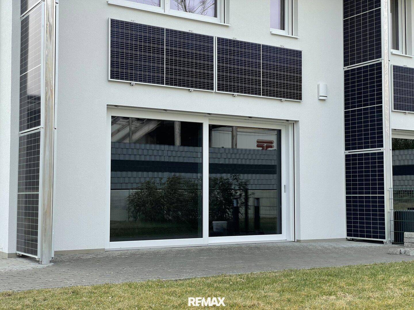 Weiße Hausfassade mit großen Schiebetüren zum Garten und installierten Solarmodulen.