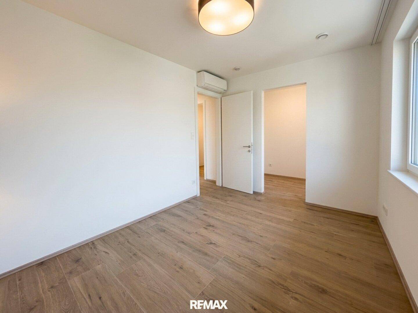 Geräumiges Schlafzimmer mit hellem Laminatboden, weiß gestrichenen Wänden und Klimaanlage.